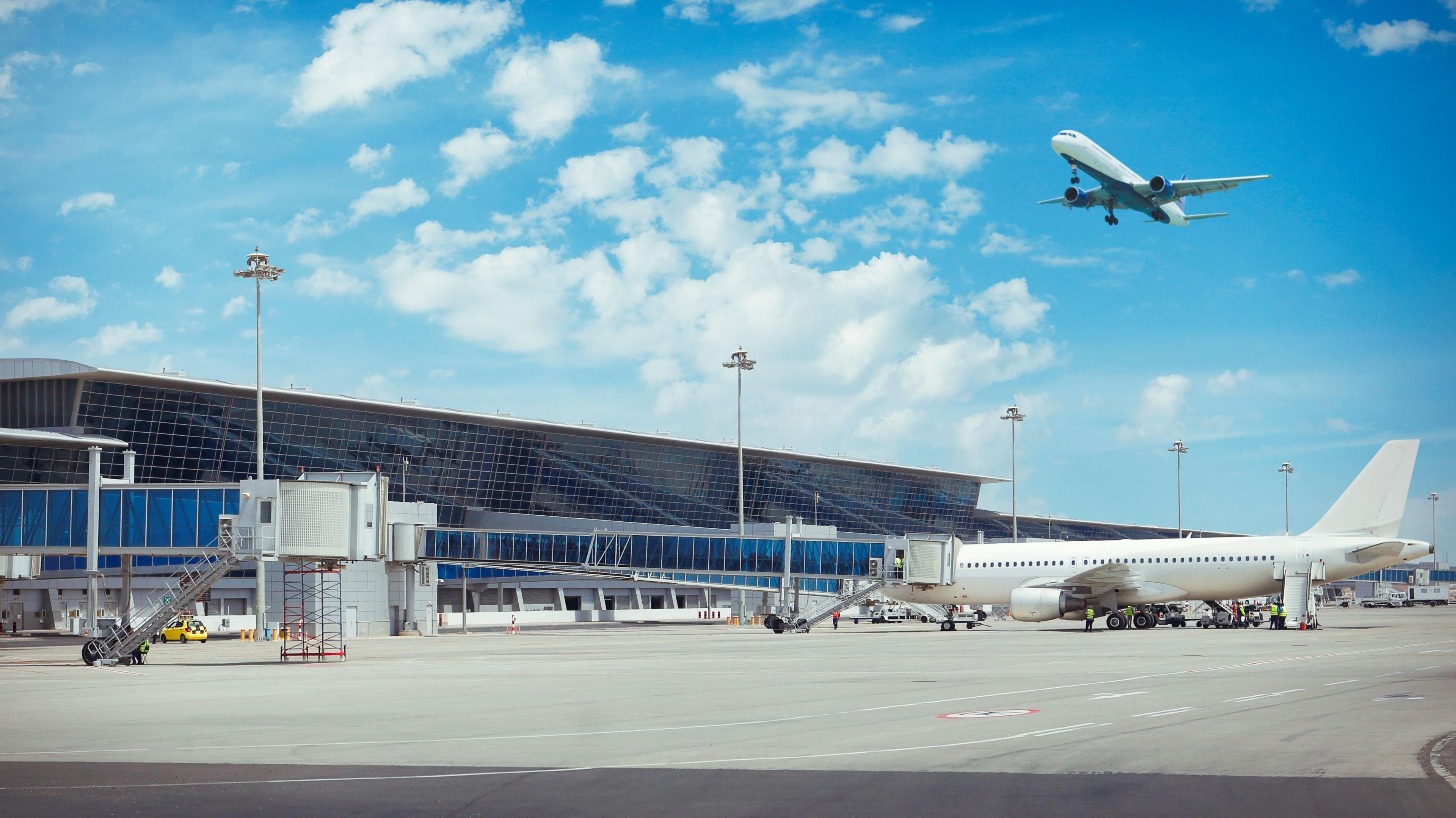 A plane in the air and a plane on tarmac at an airport.