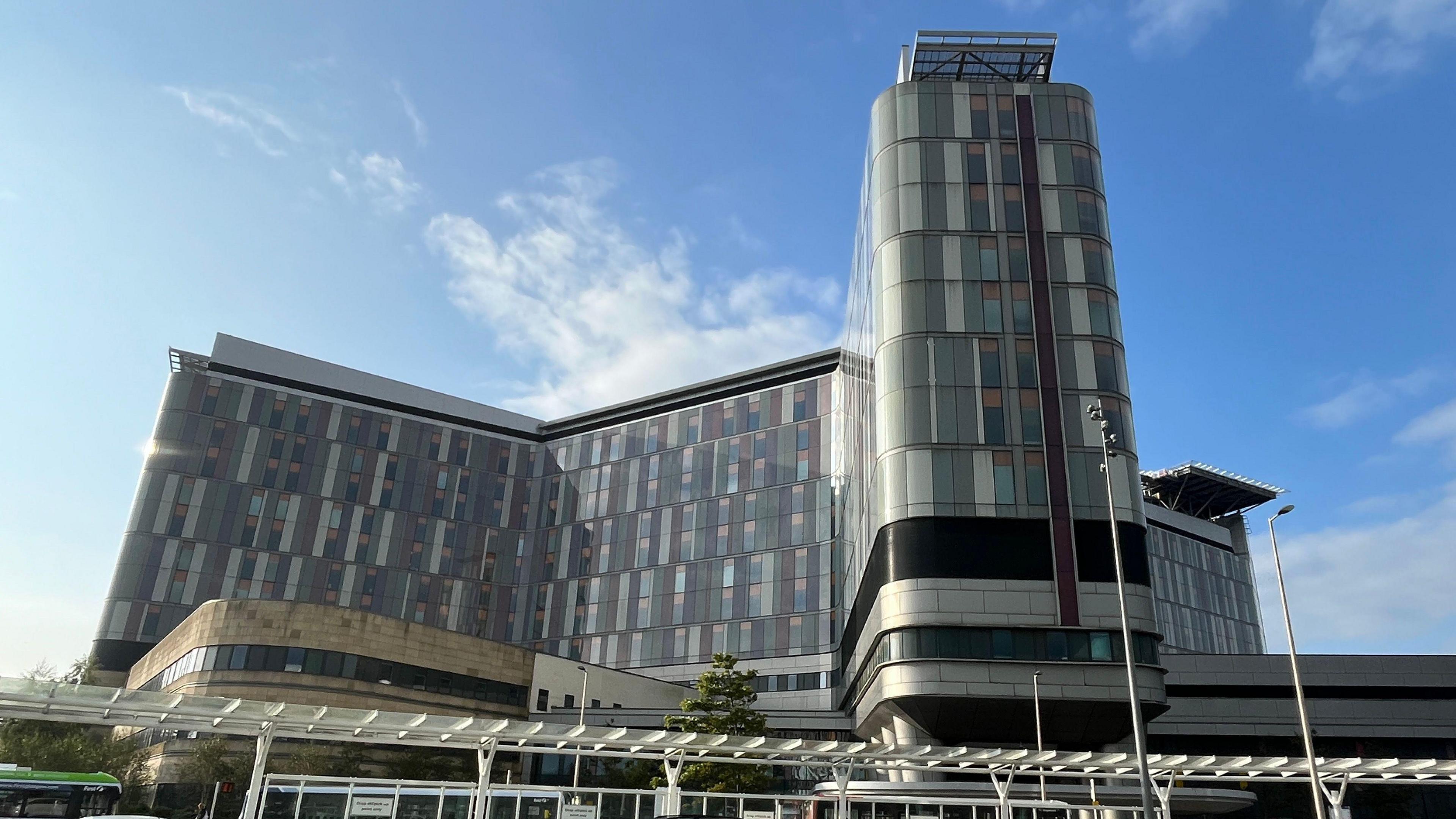 An exterior shot of the Queen Elizabeth University Hospital main building in Glasgow on a sunny day. The sky is blue with some white clouds.