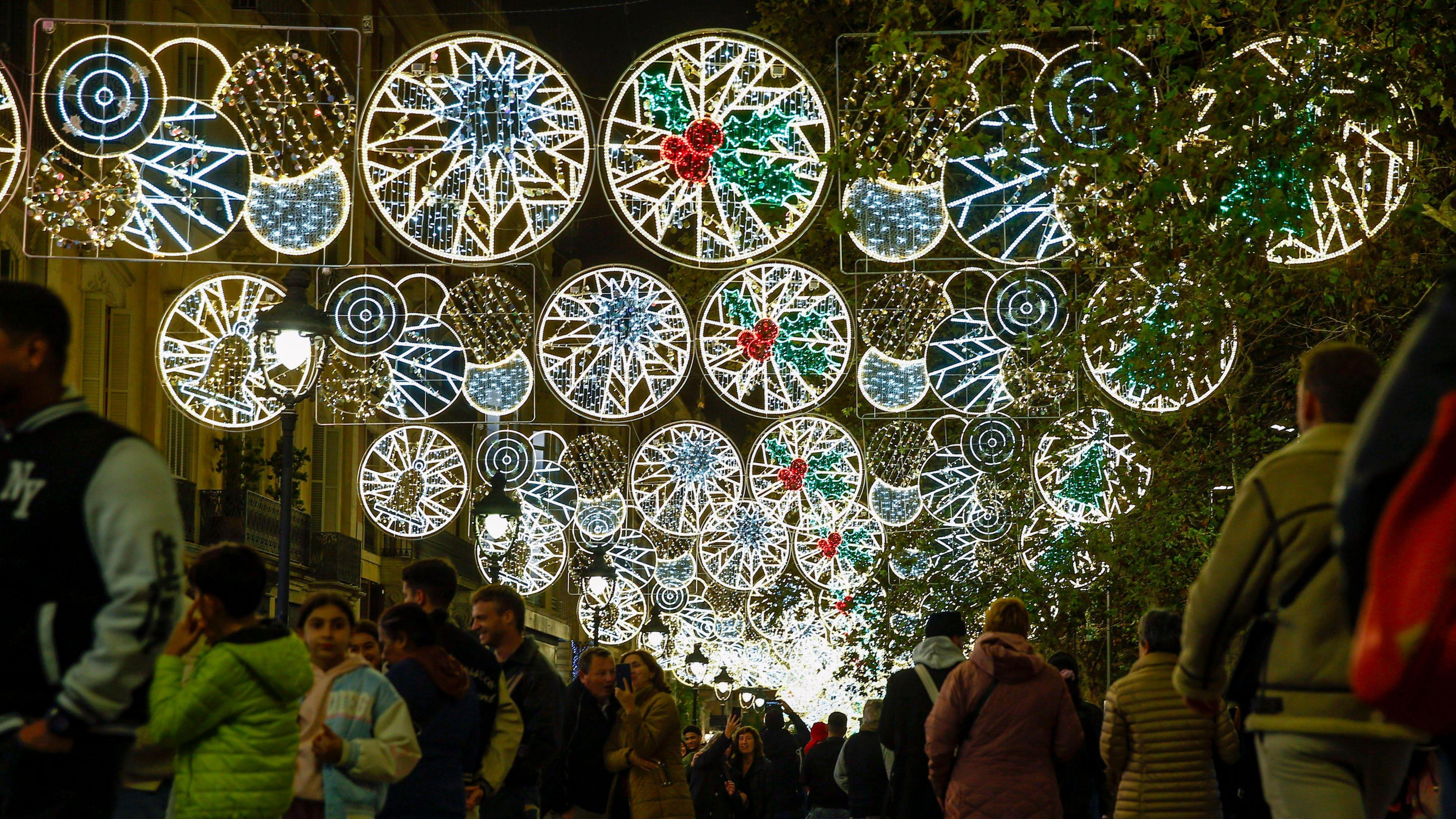 colorful circular lights featuring stars, holly leaves and berries and golden bells hang high above passersby