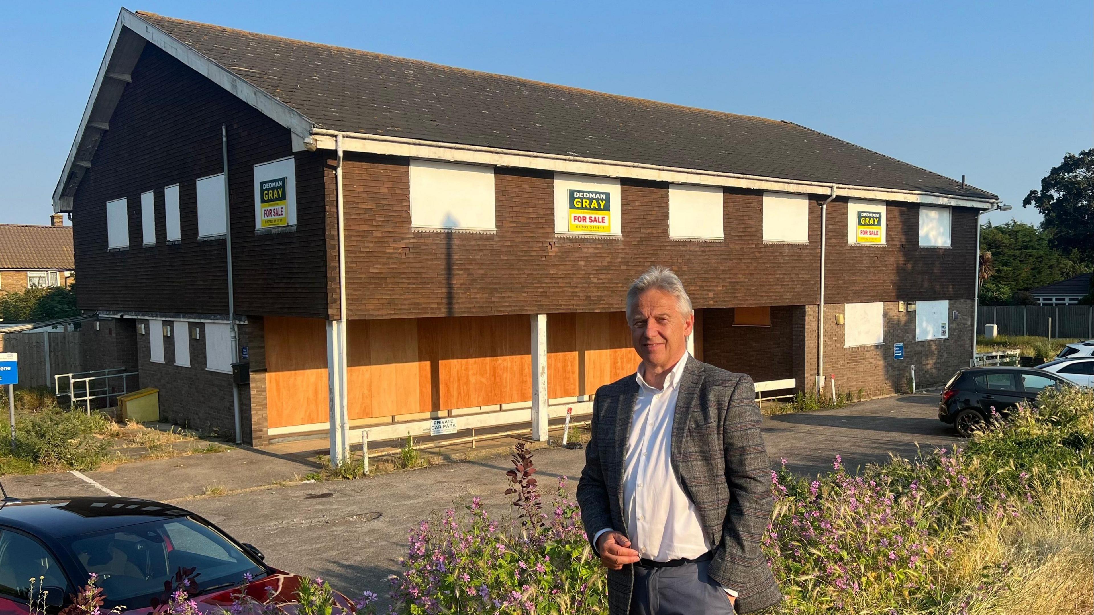 Mike Gray is wearing a blazer and standing in front of a building