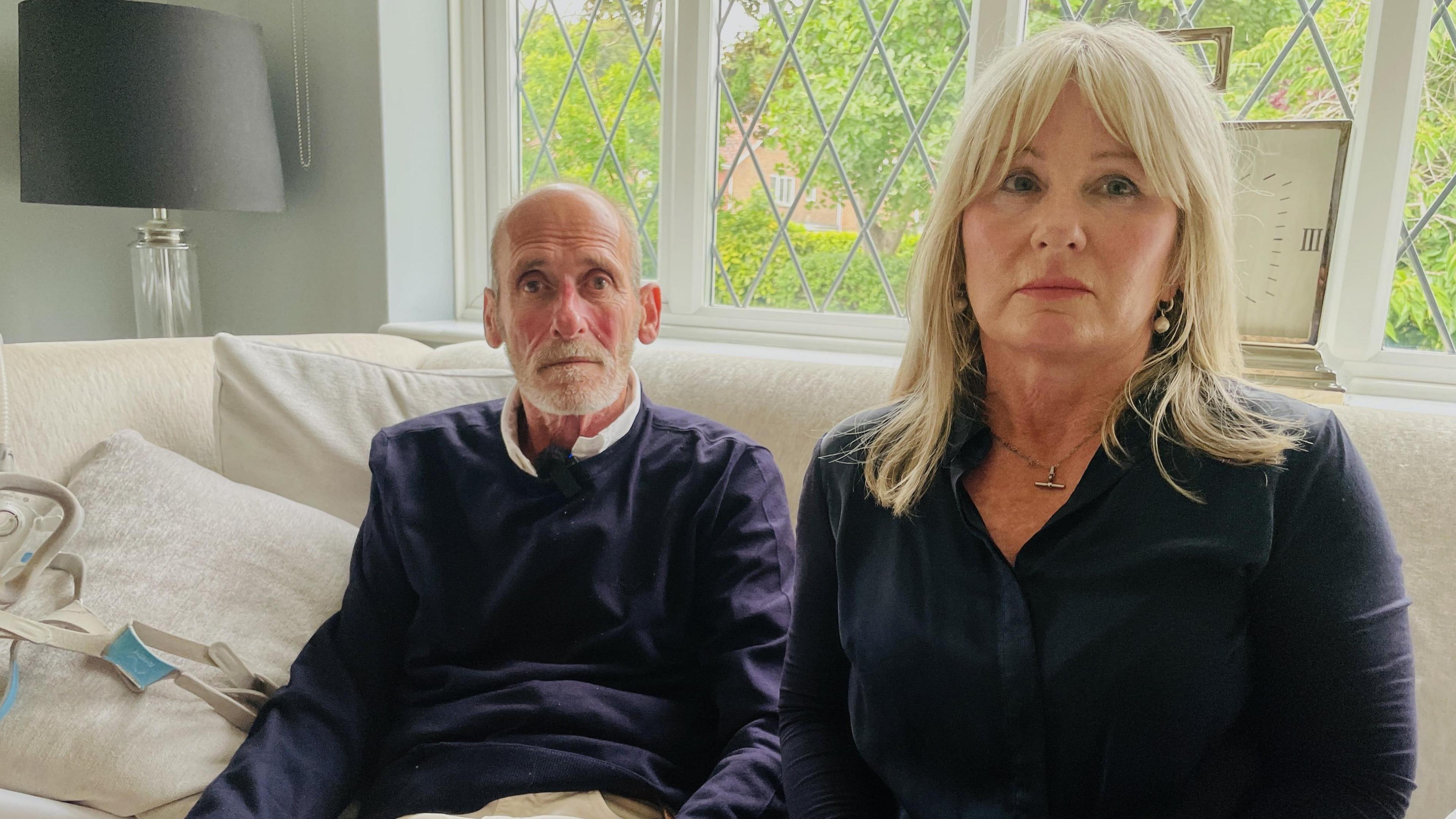 Carys and Paul Robinson sitting on a sofa with a window in the background.