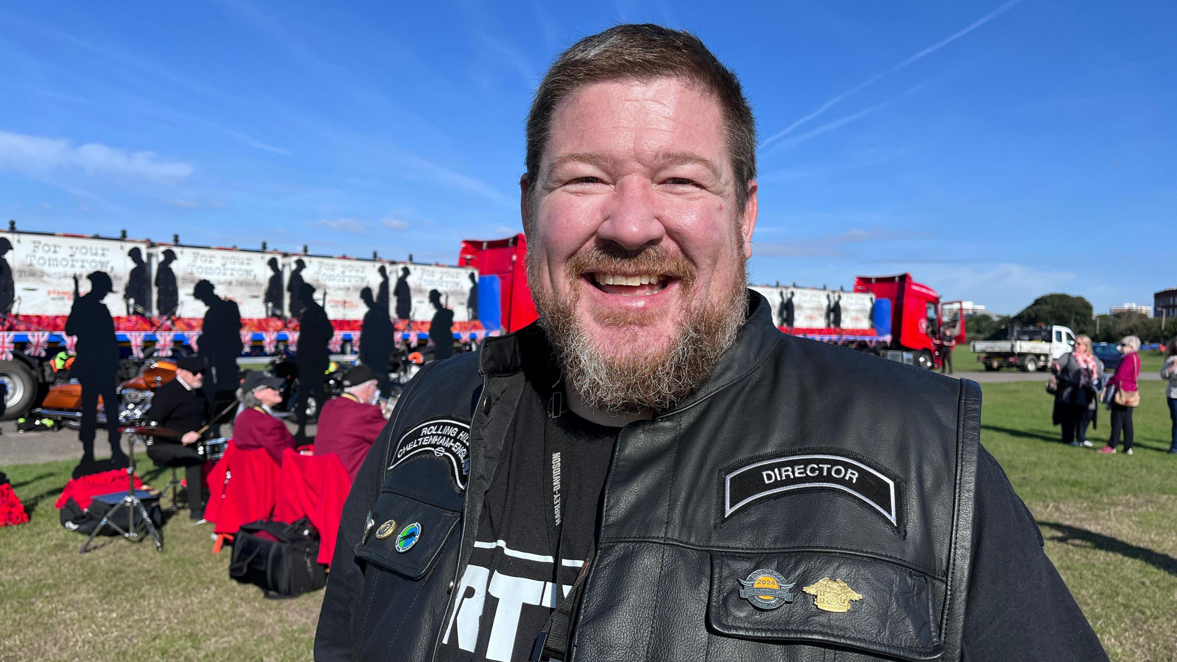 Mike smiling in his leather biker jacket and stood in front of the figures