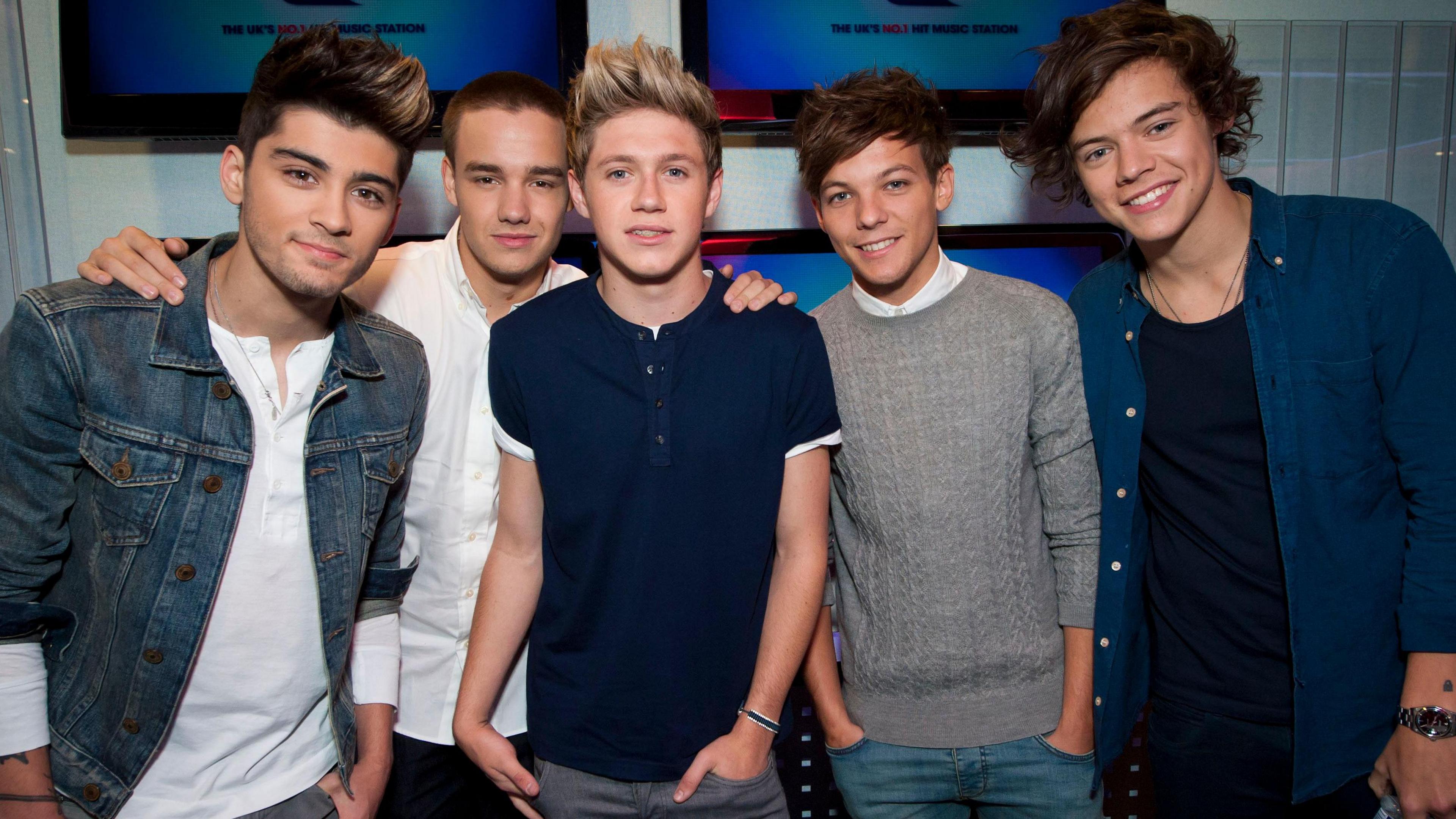 (left to right) Zayn Malik wears a denim jacket over a white t-shirt. He is stood beside Liam Payne, Niall Horan, Louis Tomlinson and Harry Styles. Liam is wearing a white shirt, Niall is wearing a navy t-shirt, Louis is wearing a grey jumper, and Harry is wearing a blue shirt over a navy t-shirt.