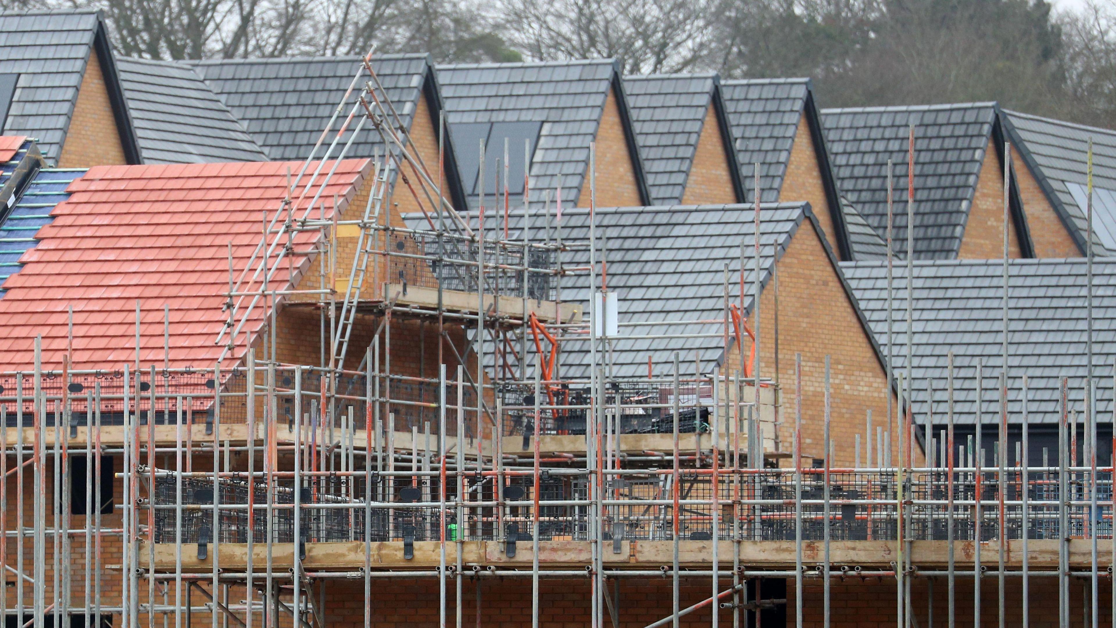 New homes under construction. The roofs of several new homes can be seen, made of red and grey slates, with scaffolding surrounding some of the homes.