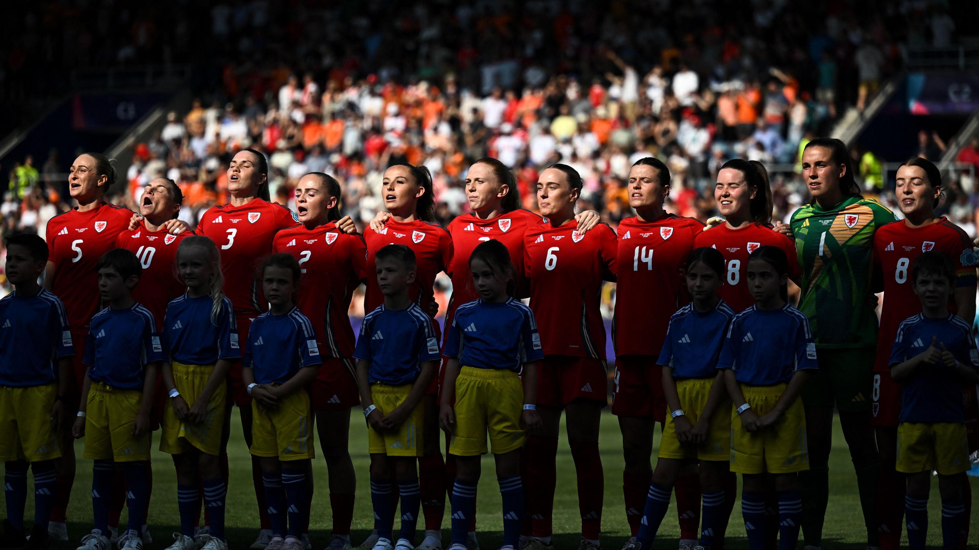 Llun o dîm Cymru'n canu'r anthem genedlaethol cyn gem yn erbyn yr Iseldiroedd ym mhencampwriaeth Ewro 2025. O'r chwith i'r dde mae Amddiffynnwr Cymru #05 Rhiannon Roberts, chwaraewr canol cae Cymru #10 Jess Fishlock, amddiffynnwr Cymru #03 Gemma Evans, amddiffynnwr Cymru #02 Lily Woodham, blaenwr Cymru #11 Hannah Cain, chwaraewr canol cae Cymru #07 Ceri Holland, amddiffynnwr Cymru #06 Josephine Green, amddiffynnwr Cymru #14 Hayley Ladd, amddiffynnwr Cymru #18 Esther Morgan, gôl-geidwad Cymru #01 Olivia Clark, chwaraewr canol cae Cymru #08 Angharad