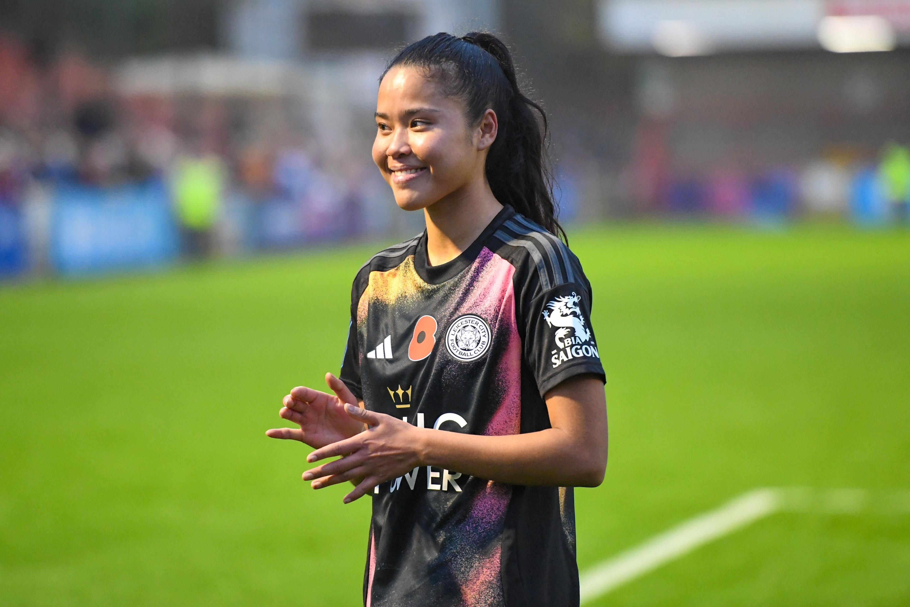Asmita Ale sonríe y aplaude en un campo de fútbol. Lleva una camiseta rosa y negra y el pelo negro recogido.