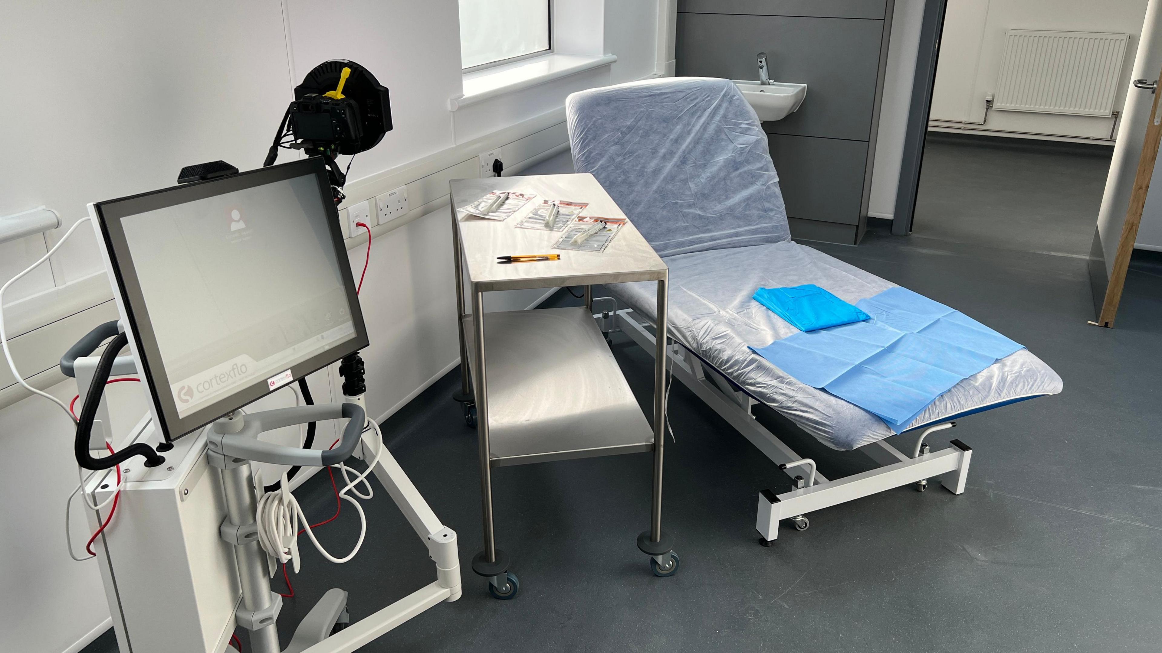 A medical bed with a silver trolley and a screen next to it.