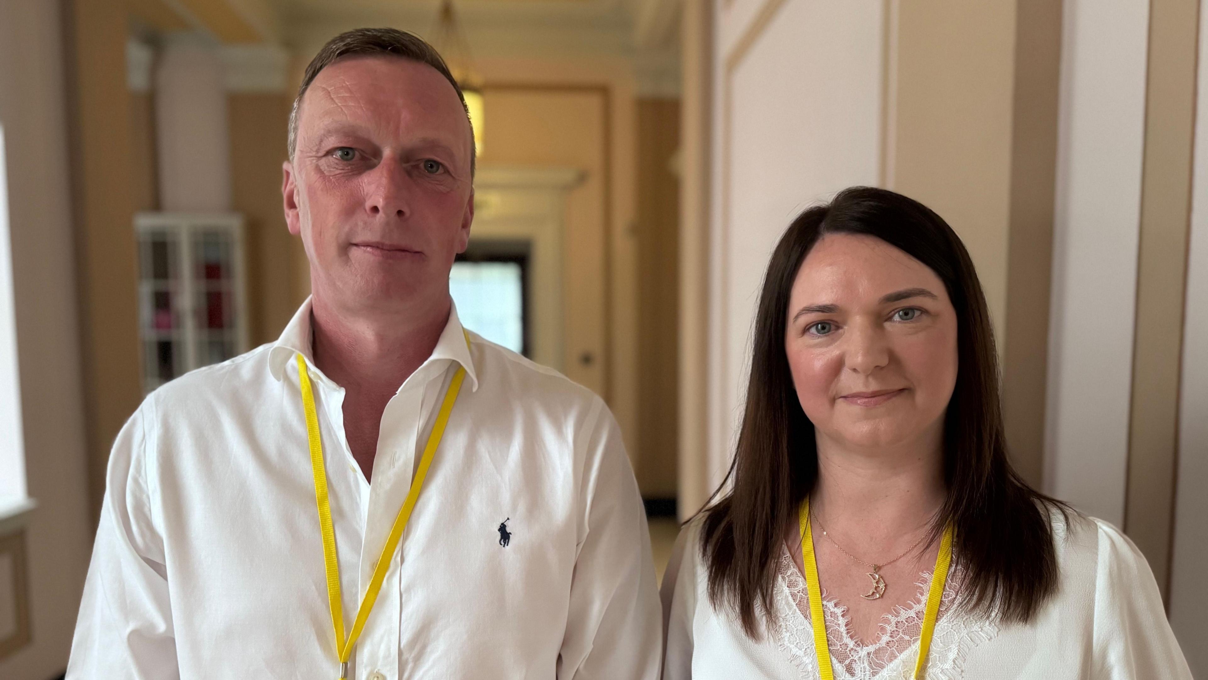 Neville and Joanne Reid. Neville has short brown hair, wearing a white shirt and yellow lanyard. Joanne has dark shoulder length hair, wearing a sliver moon necklace, white top and yellow lanyard.