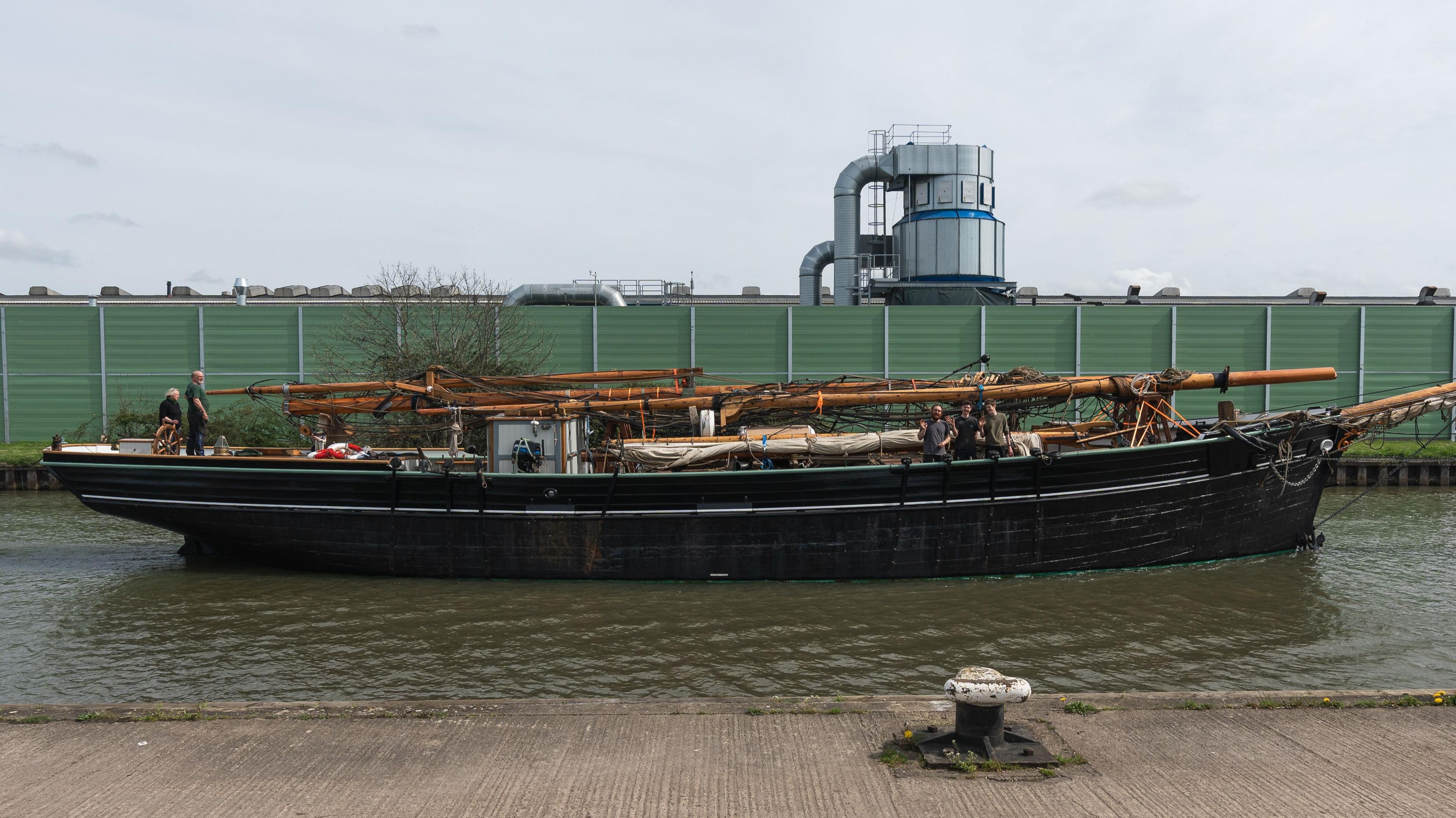 A traditional tall ship with its masts laid flat on the deck travels up the Gloucestershire and Sharpness canal.  