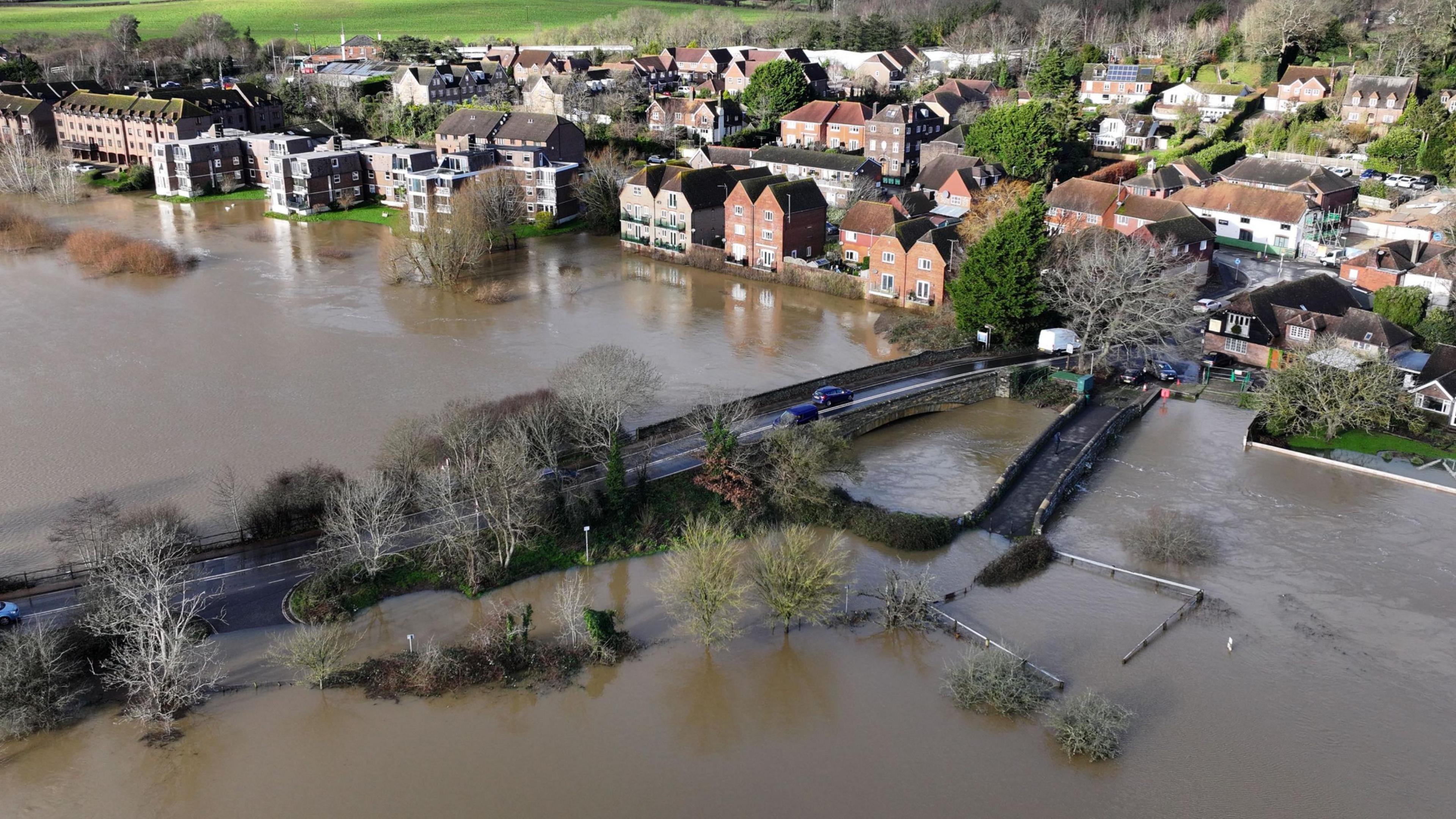 An aerial shot of fields surrounding a town which are completely flooded. A road bridge cuts through the flooding. 