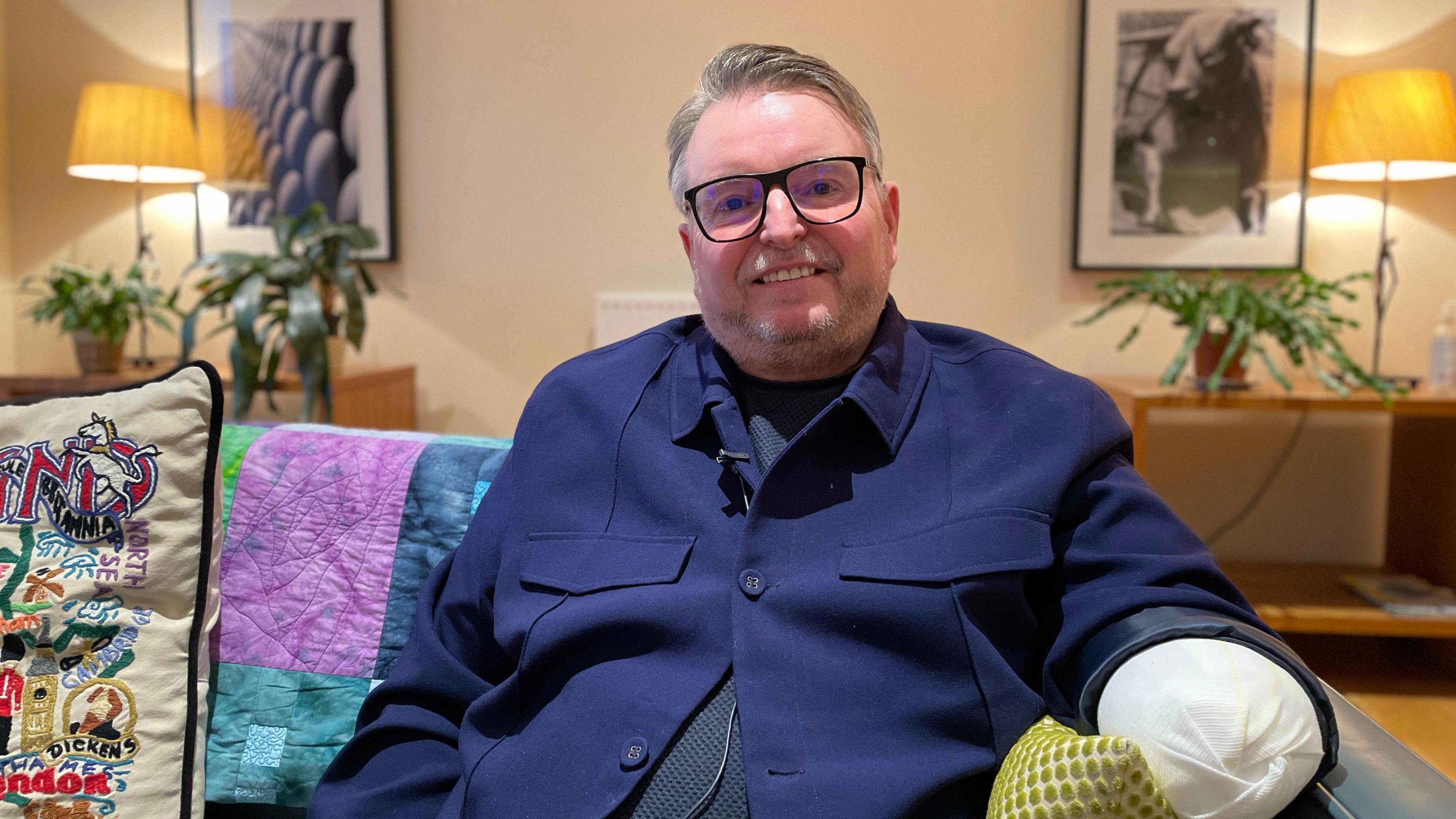 Matt Davies is pictured at Fisher House, the hospital's home away from home for injured military staff. He is sat on a sofa, which has colourful cushions on it, and is wearing a blue jacket.