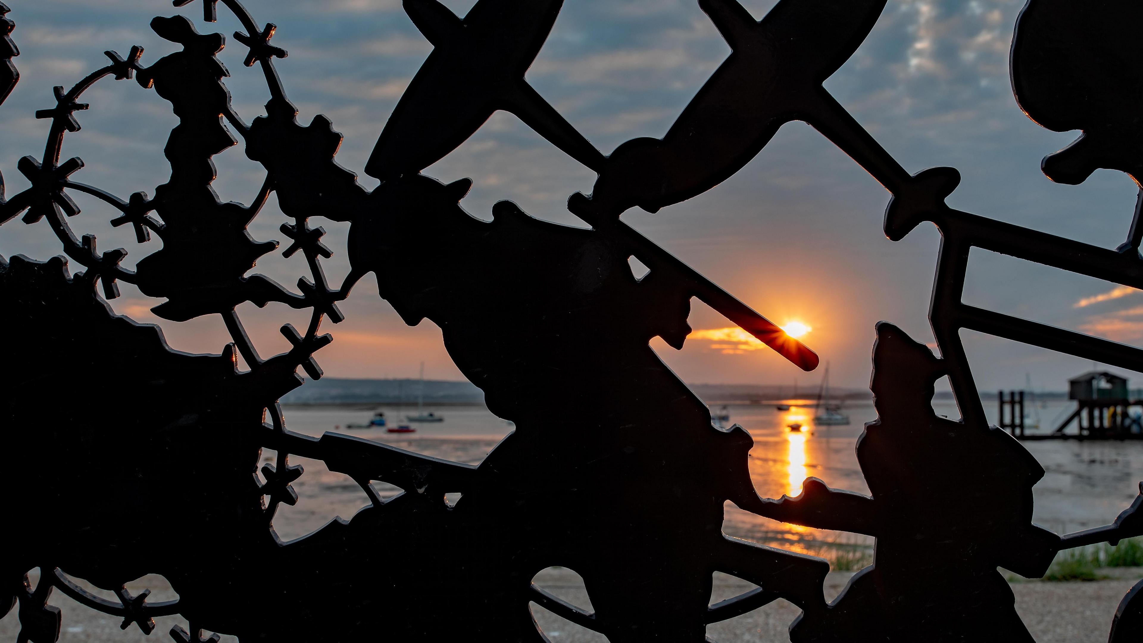 Metal artwork of a soldier, Spitfire aeroplanes and barbed wire in darkness with a sunrise over the English Channel in the background