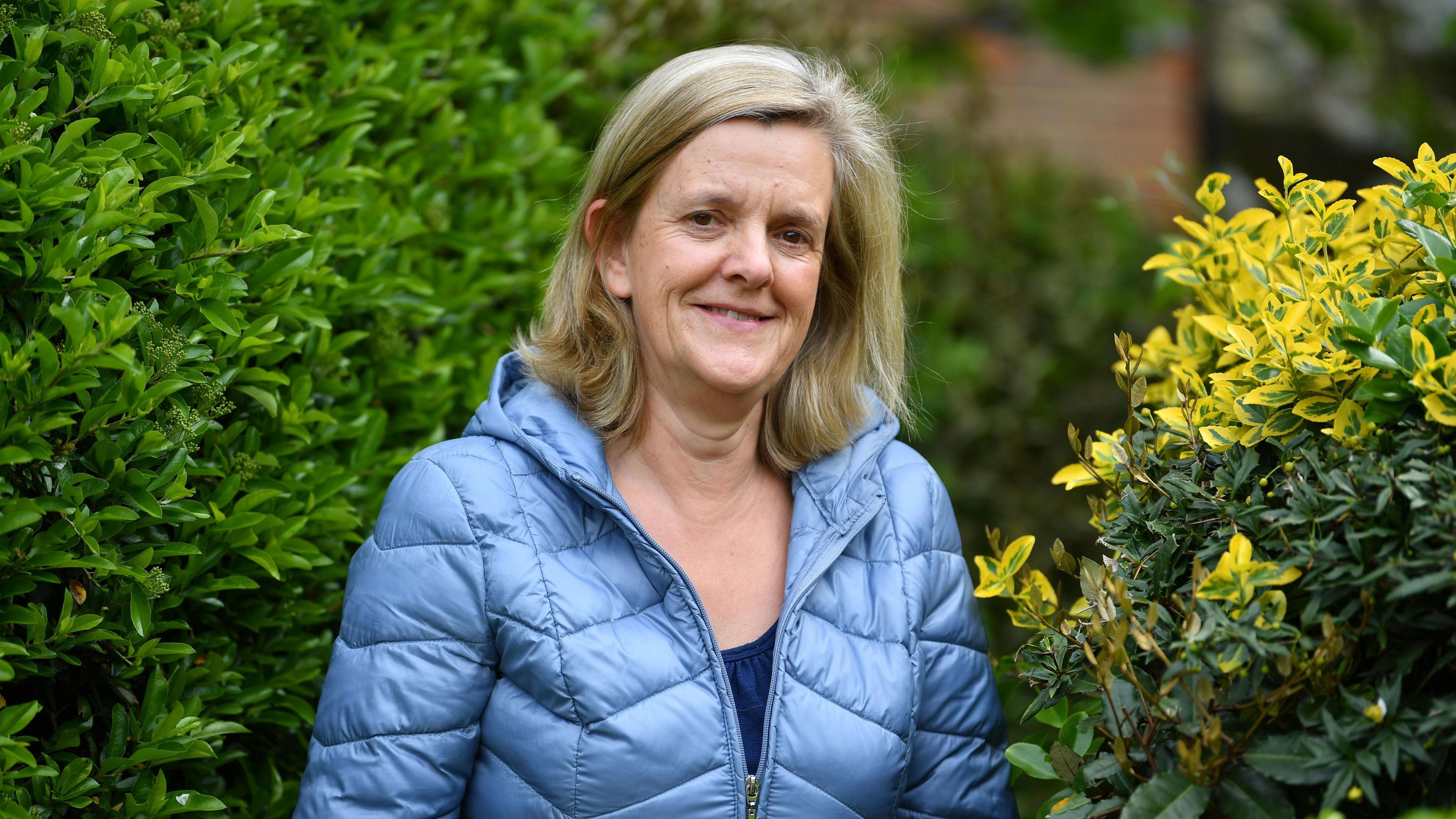 Catherine Sayer, leader of Tandridge District Council, wearing a blue coat and standing in front of a green bush.