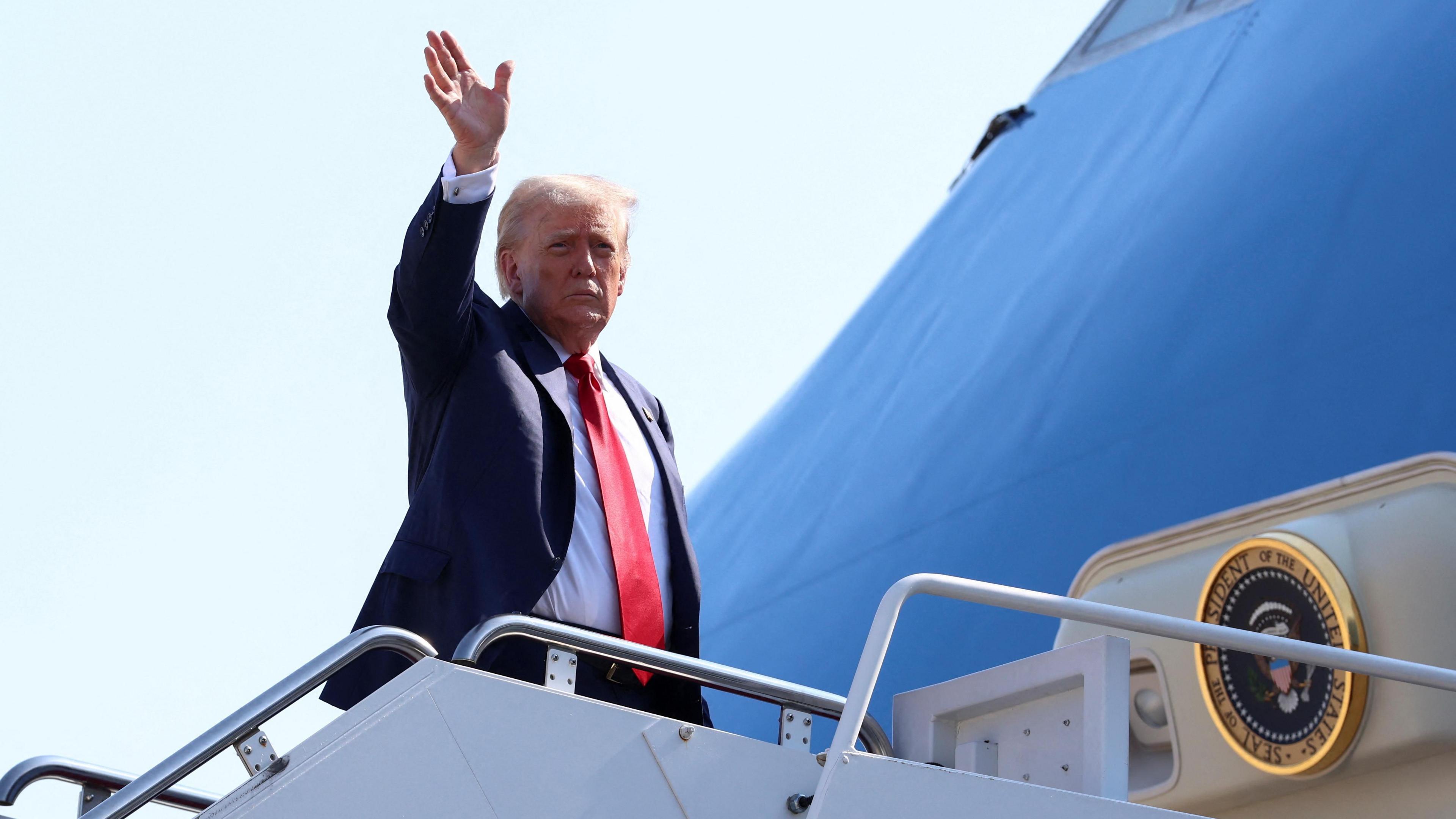 Donald Trump, wearing a dark suit, white shirt and red tie, waves as he emerges from the presidential plane Air Force One.