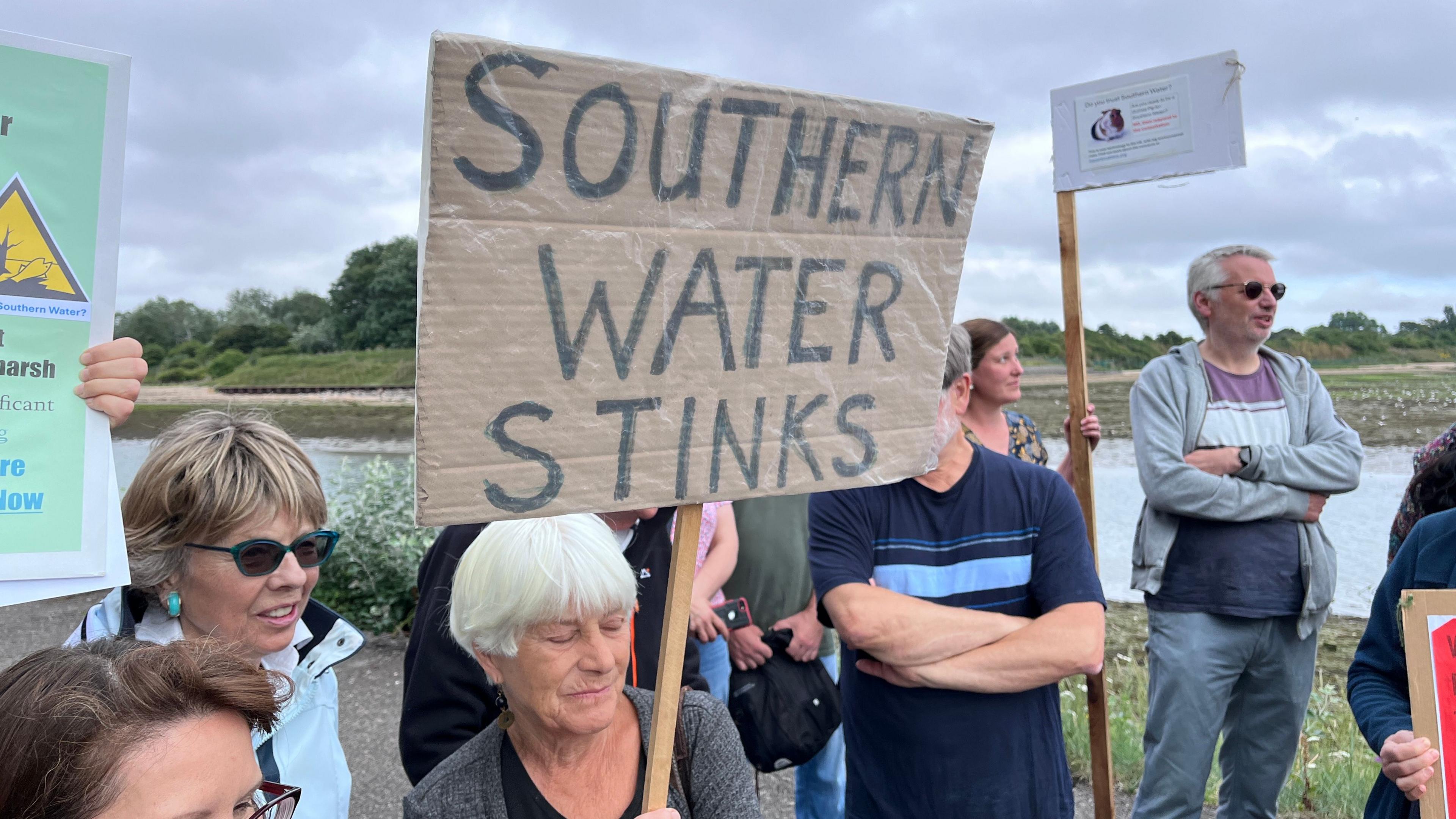 Photo showing several people gathering by waterfront with banners - one says Southern Water Stinks