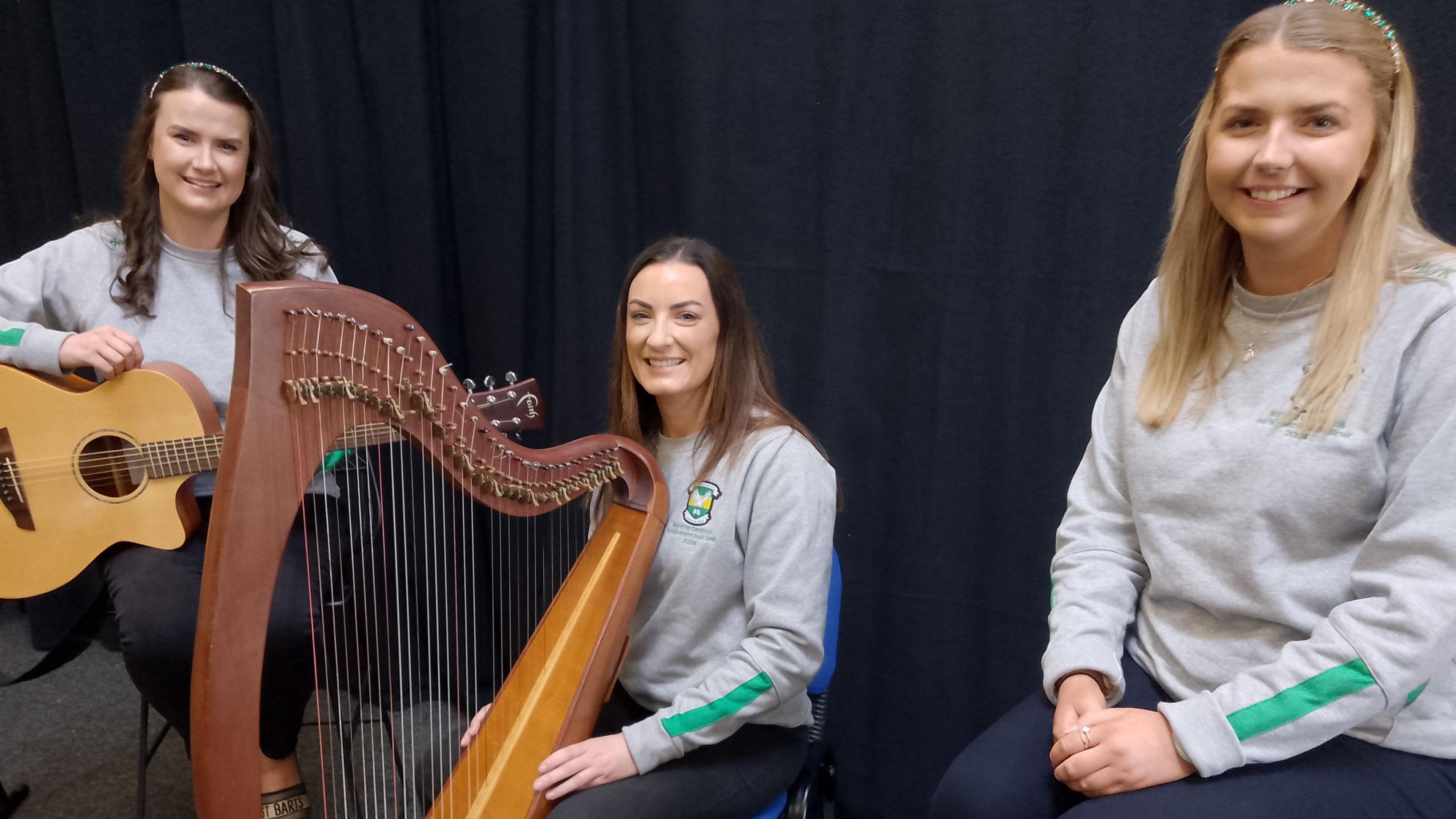 All-Ireland ballad group champions. Rachel Mitchell is posing with her guitar. One of her teammates has a harp and a third teammate is sitting with her hands in her lap