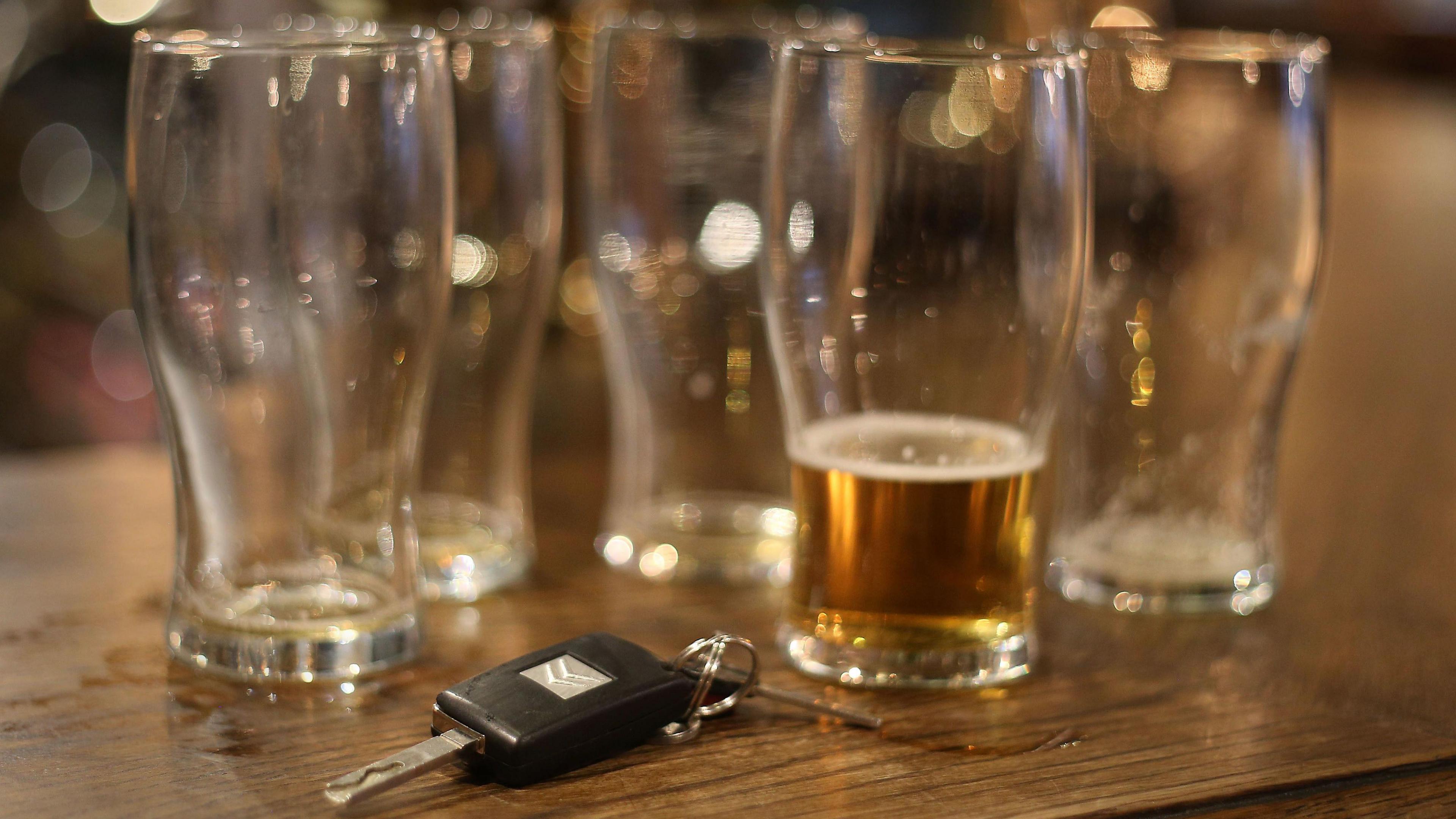 Several empty pint glasses rest on a pub table. One is still partly filled with beer while a car key sits next to it.