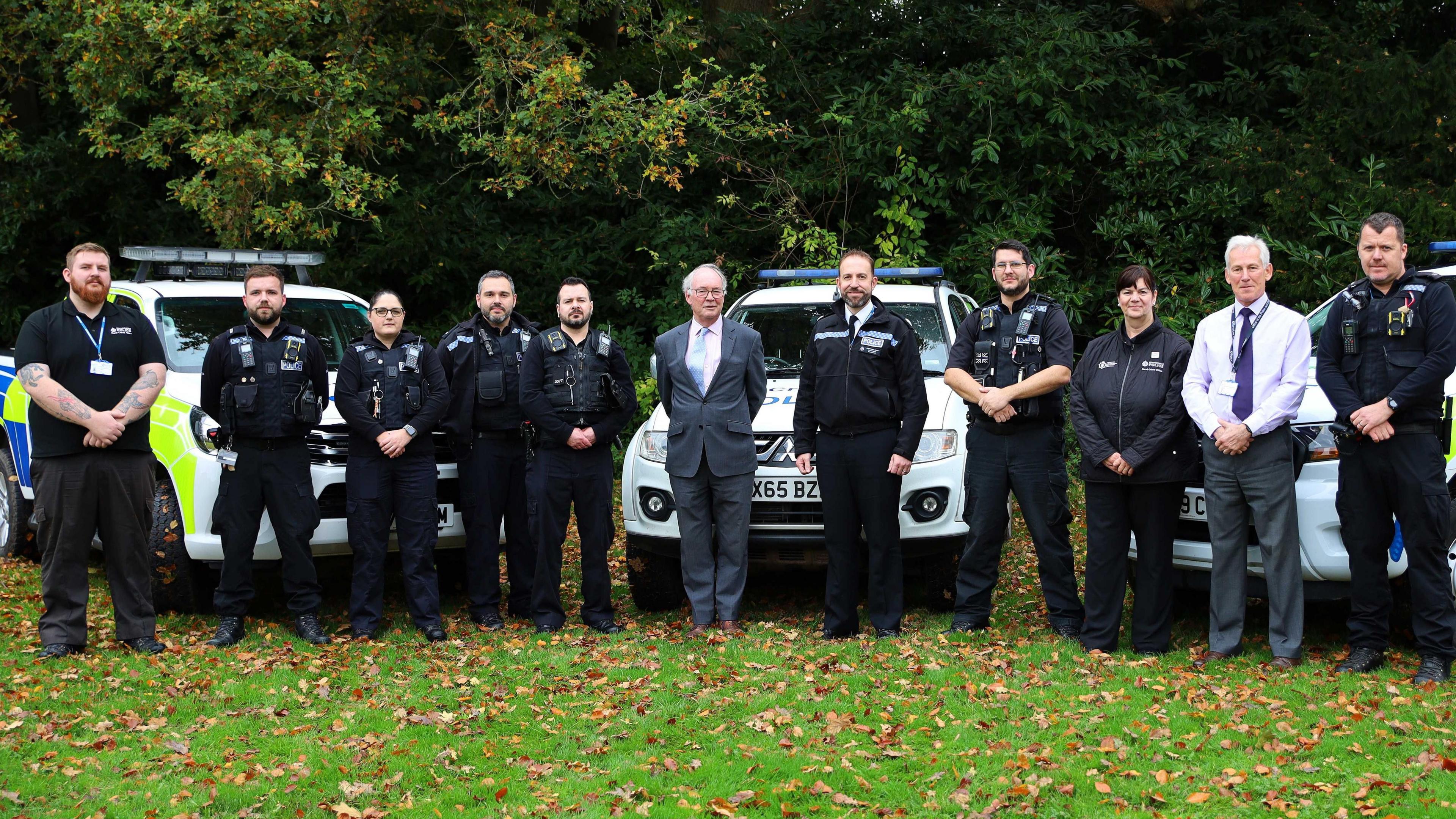 Police and Crime Commissioner Philip Seccombe in  suit standing with ten officers from the rural crime team. They are in a field. 