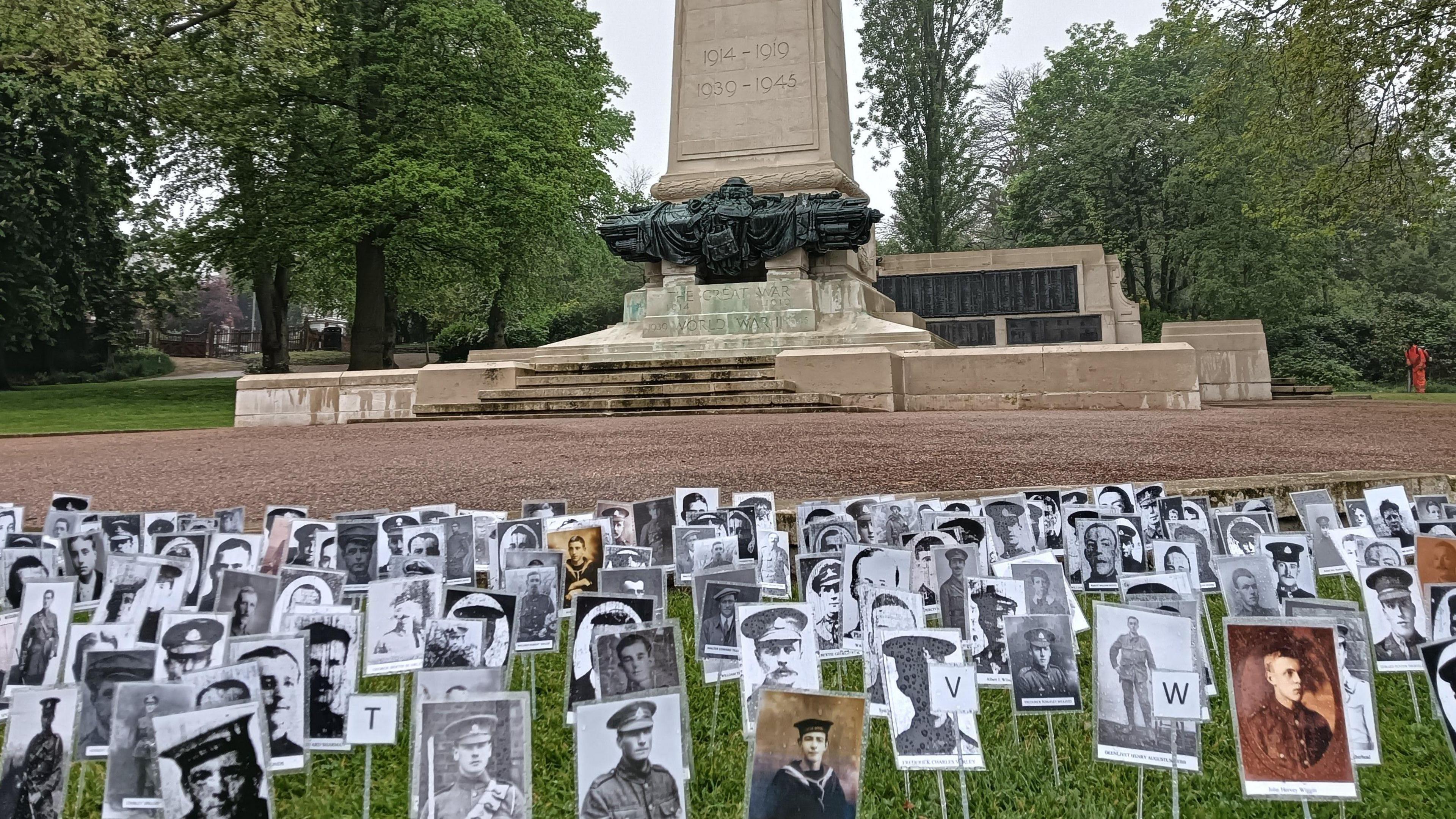 Tens of portraits of men and women lost in wars are placed in the grass in front of Ipswich's war memorial and cenotaph. The portraits have been placed on sticks and placed into the ground. 