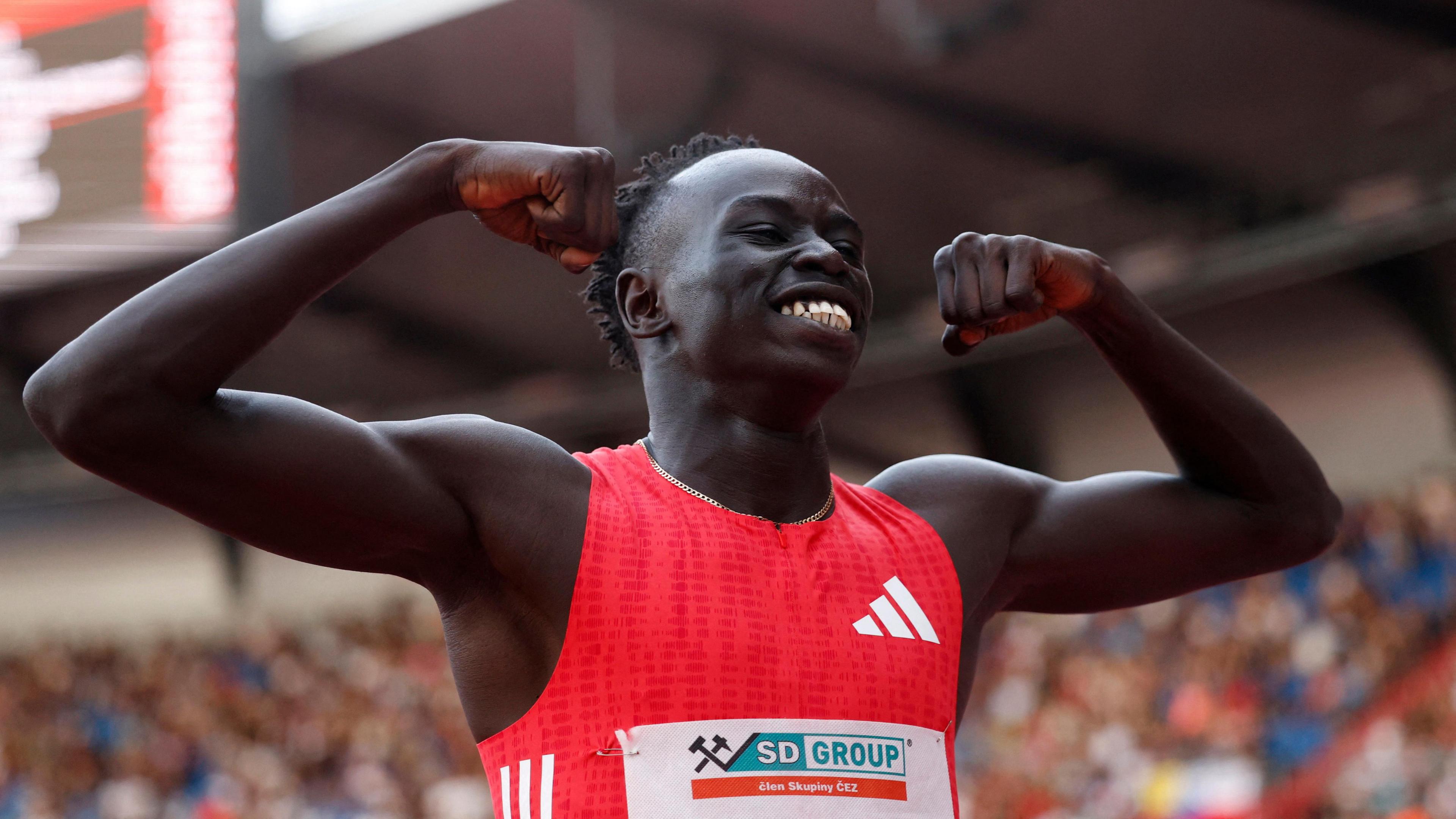 Gout Gout wears a red running top and holds his arms up in a stadium
