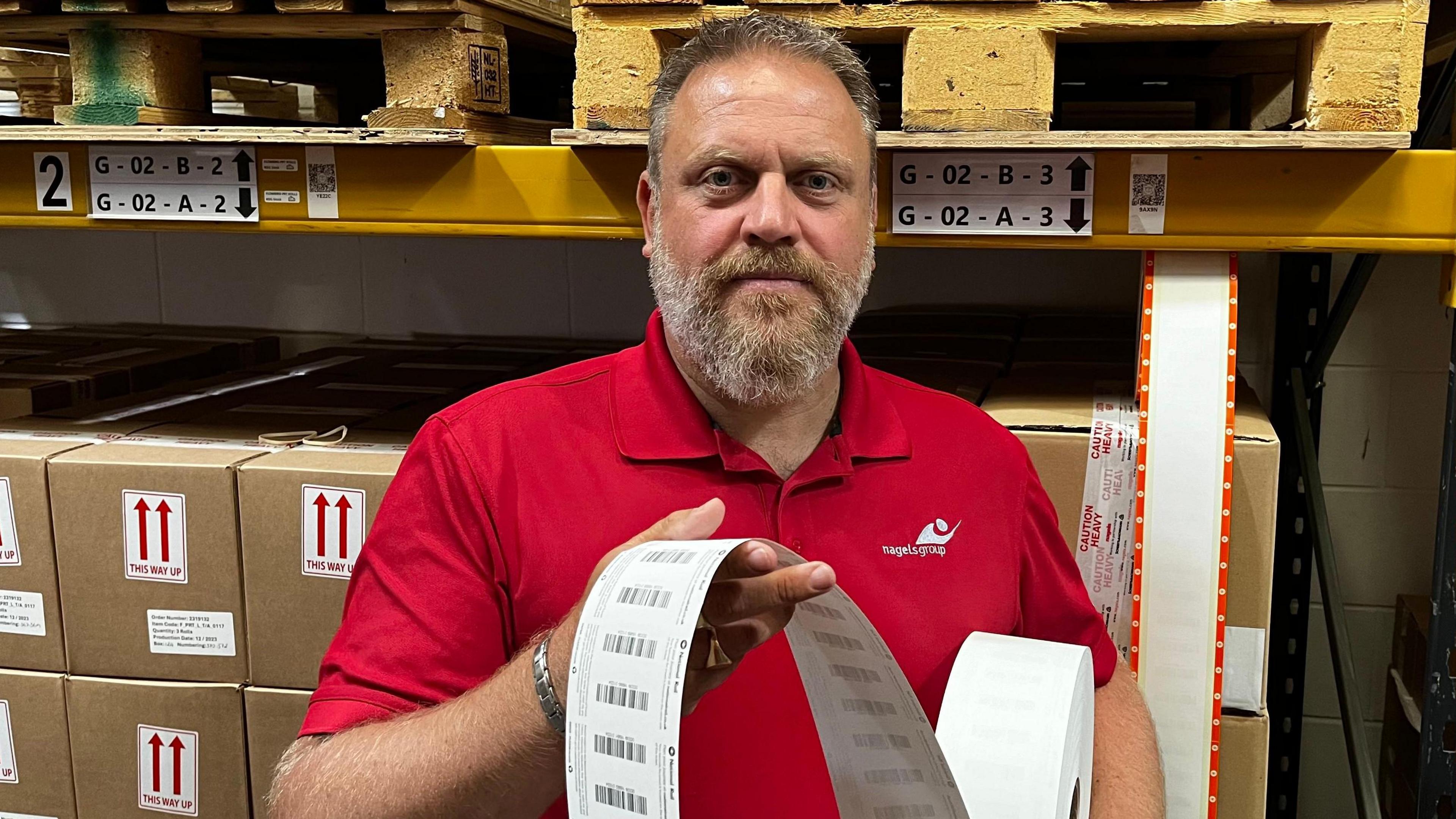 Lee Minter holding a roll of tickets, standing in front of some boxes