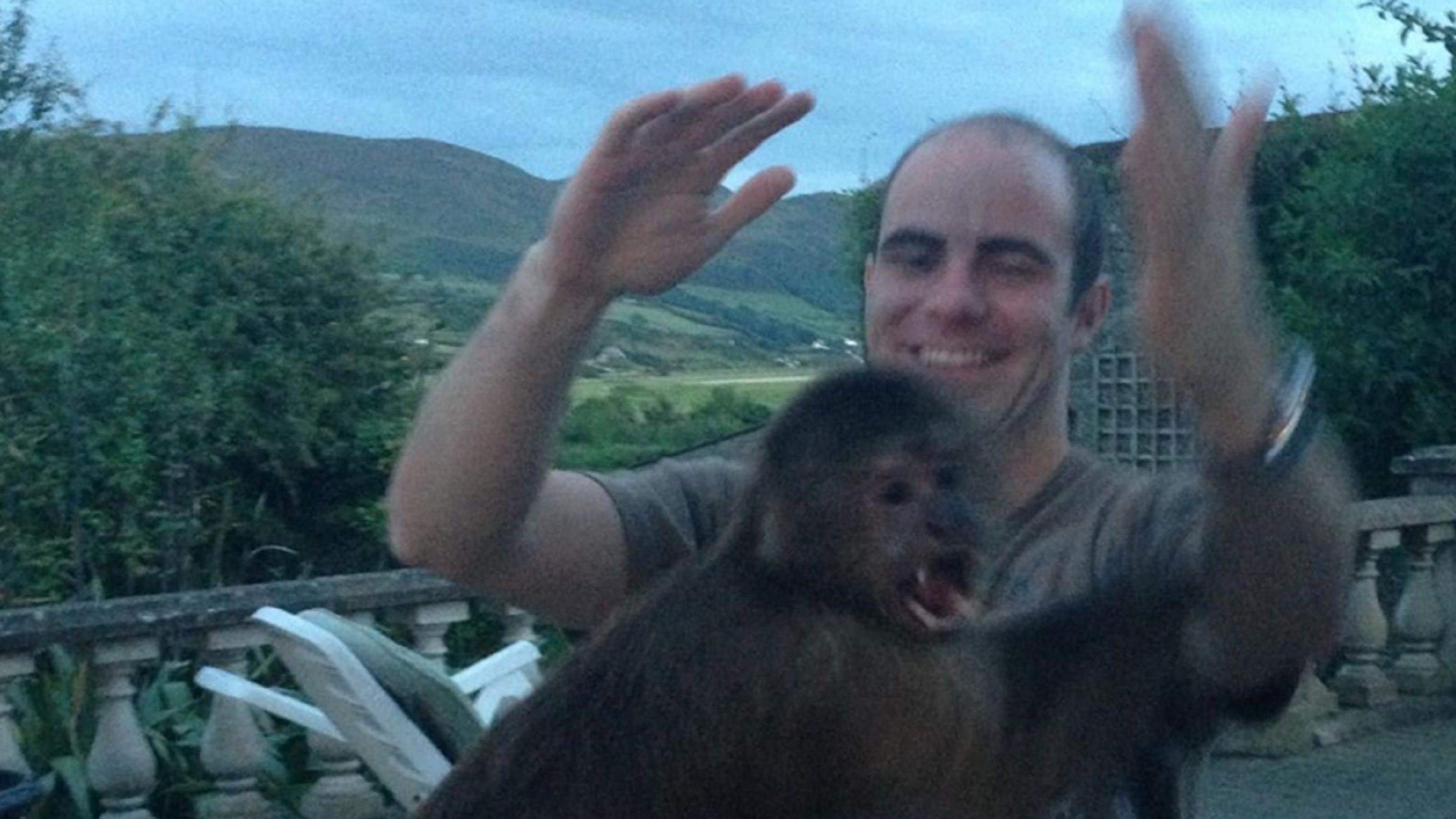 Killian McLaughlin has receding black hair. He is smiling and waving his hands in the air. Joey has dark brown fur and is sitting in front of Mr McLaughlin.