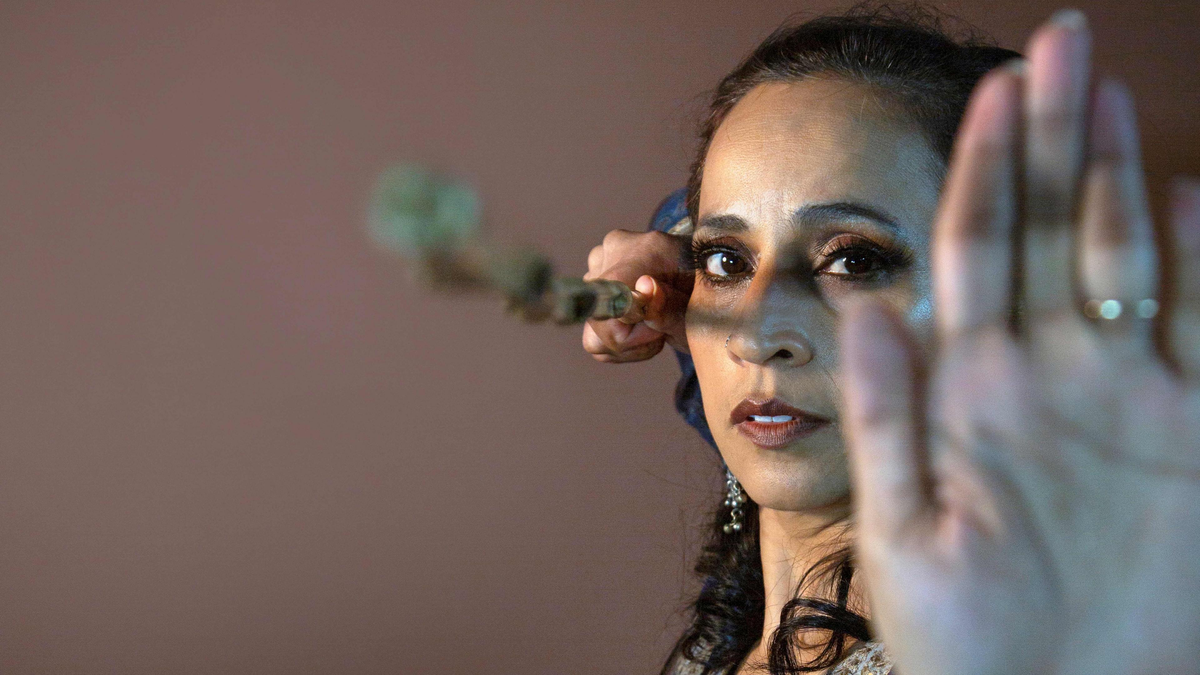 Urja Desai Thakore with one arm held up to the camera in a dance pose, the other arm is holding a prop. 