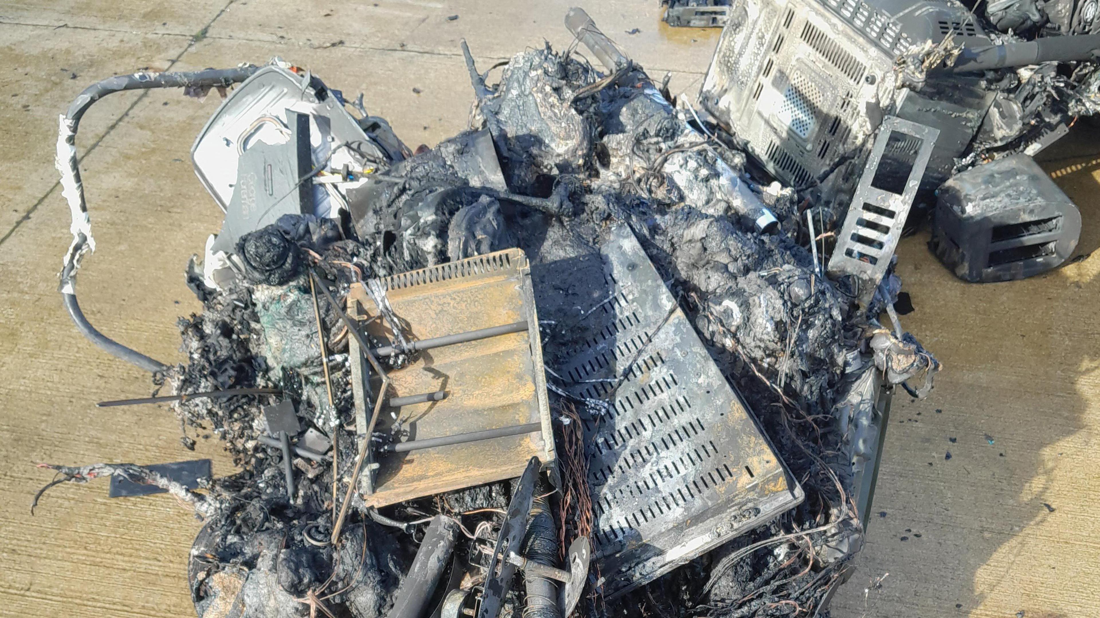 Damage of electrical items caused by fire - a cluster of grey coloured items burnt up in a pile. They have been placed on the ground.