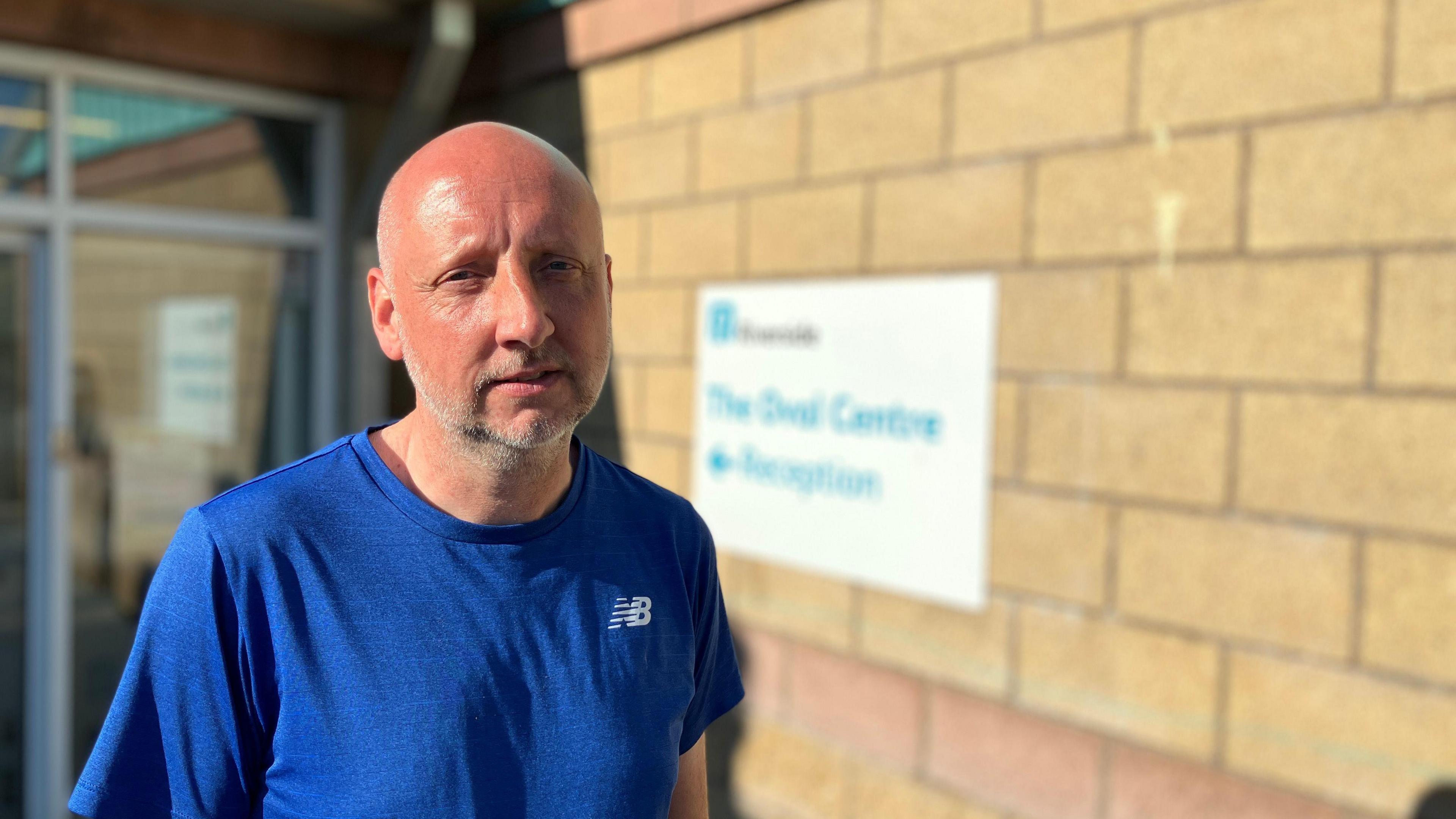 Participant Nathan Staniford, who is bald and wears a blue T-shirt, standing outside a building.