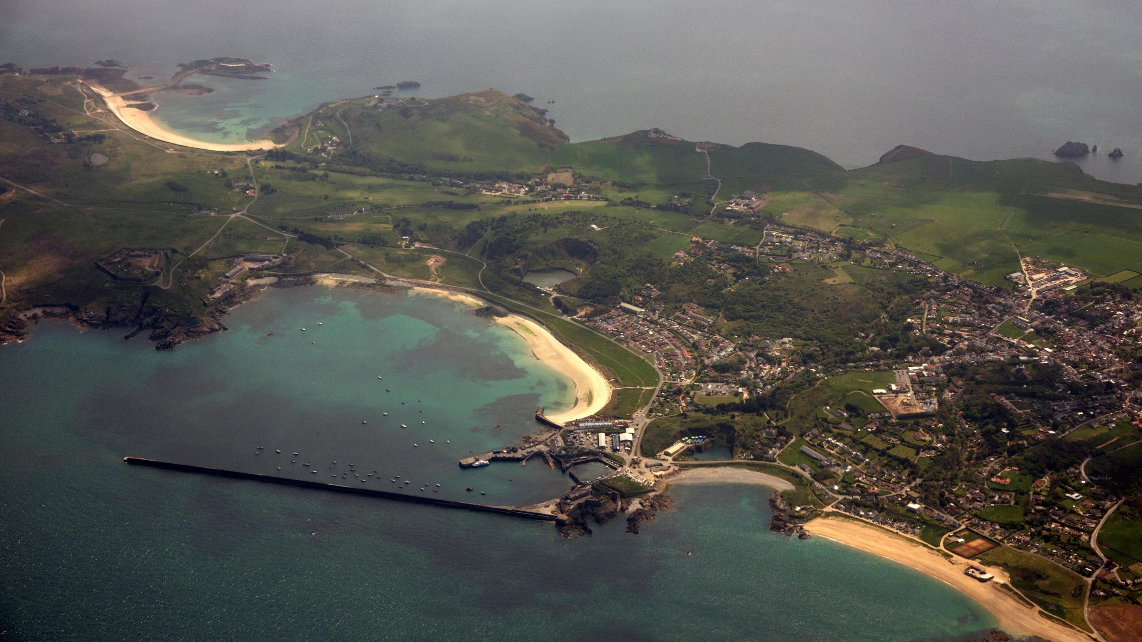 An aerial view of Alderney showing a harbour, housing and green fields. 