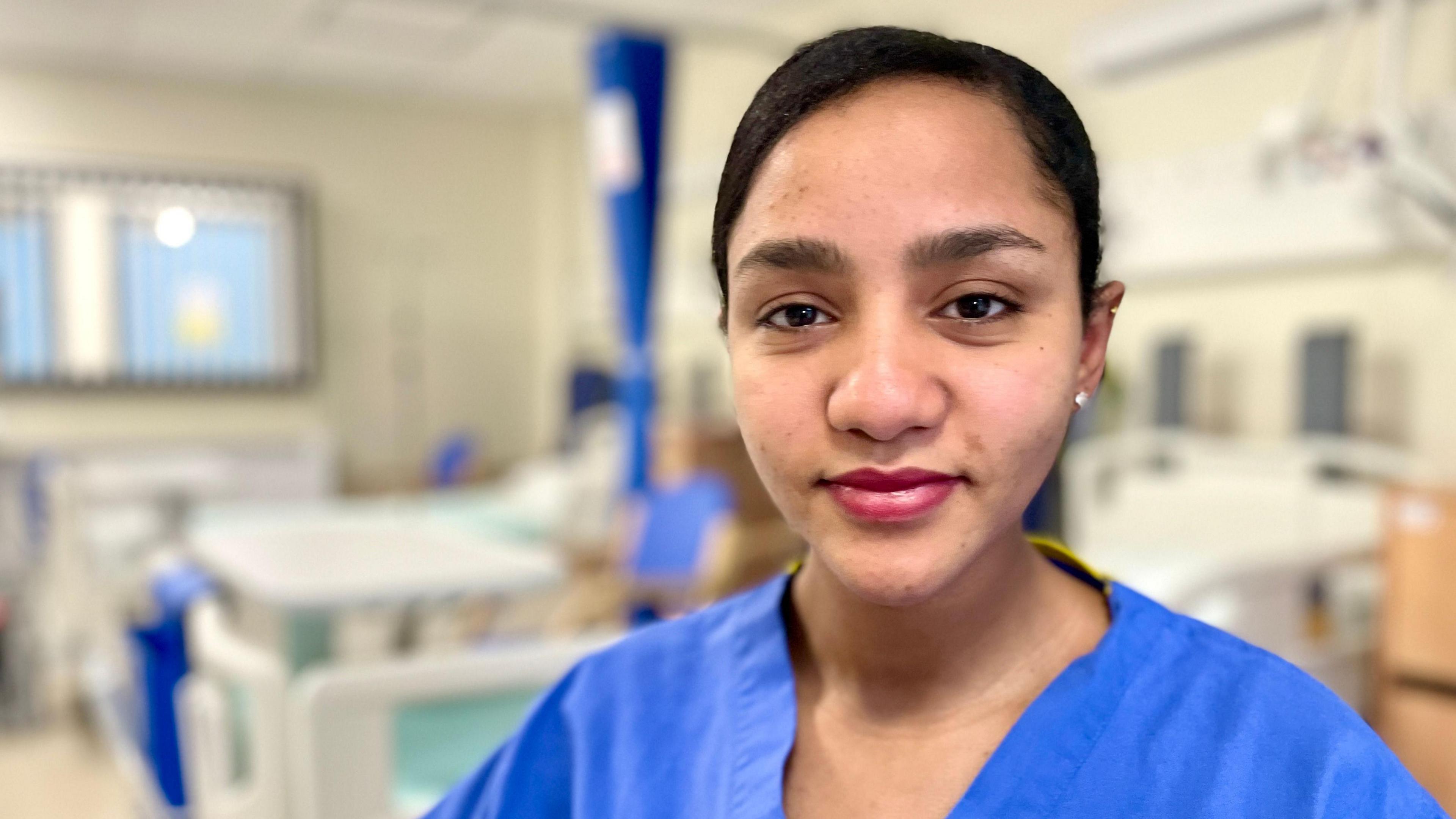 Rishan Belete wearing nurses scrubs and looking at the camera with hospital beds in the background