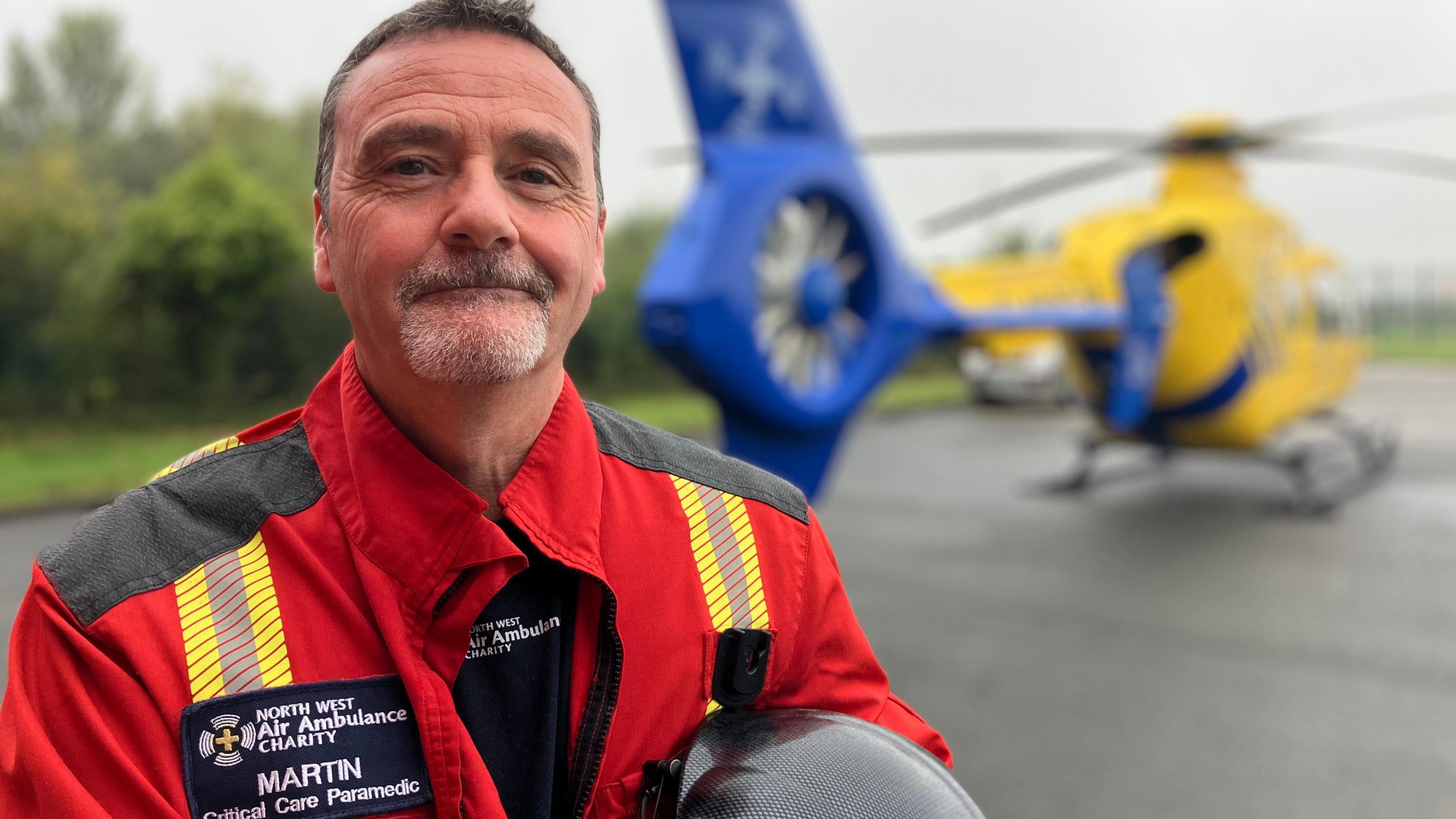 Martin Booth wearing a red and yellow uniform in front of the air ambulance