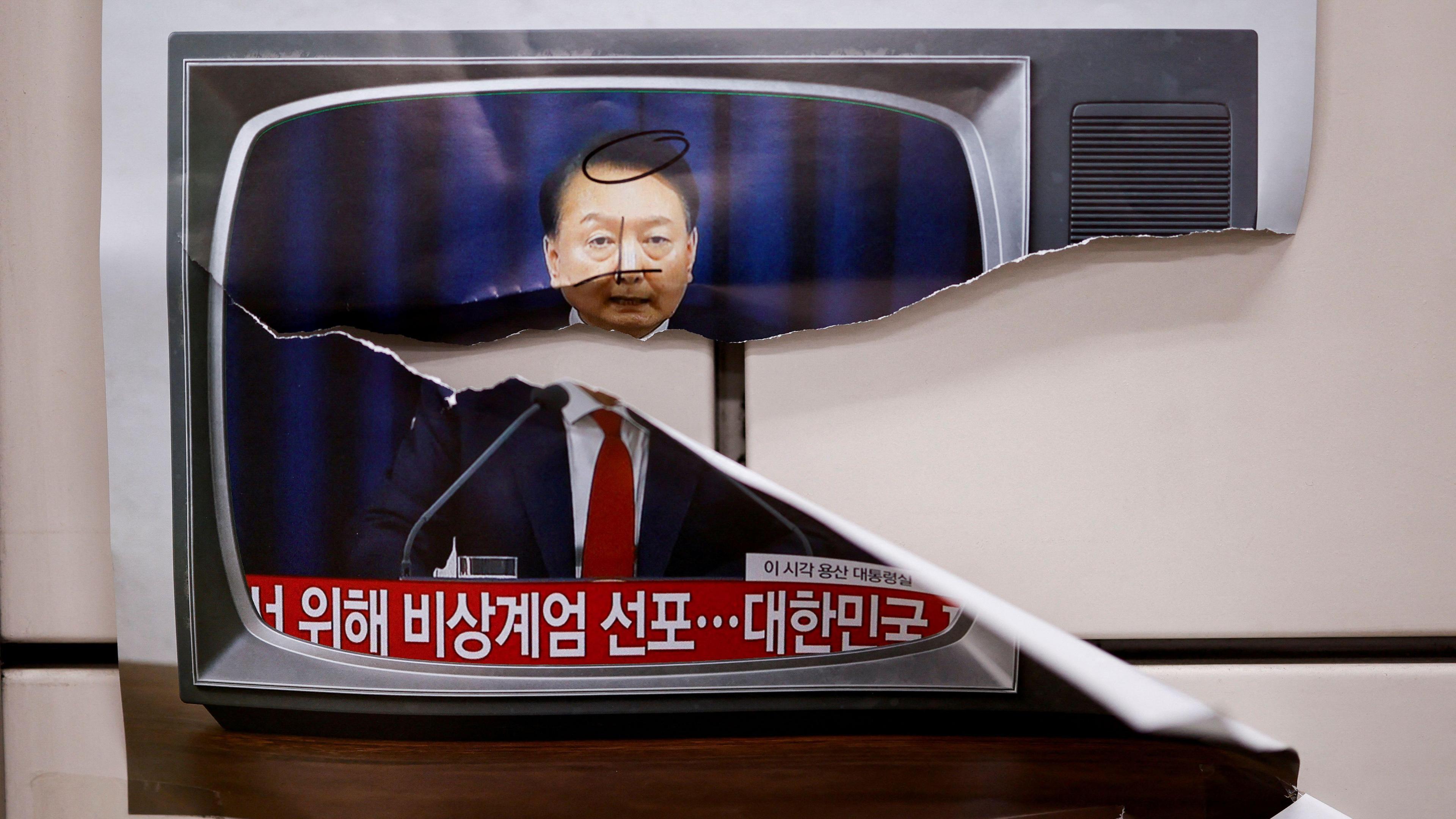 An image of South Korea's president on a TV screen, with a big tear through the middle.