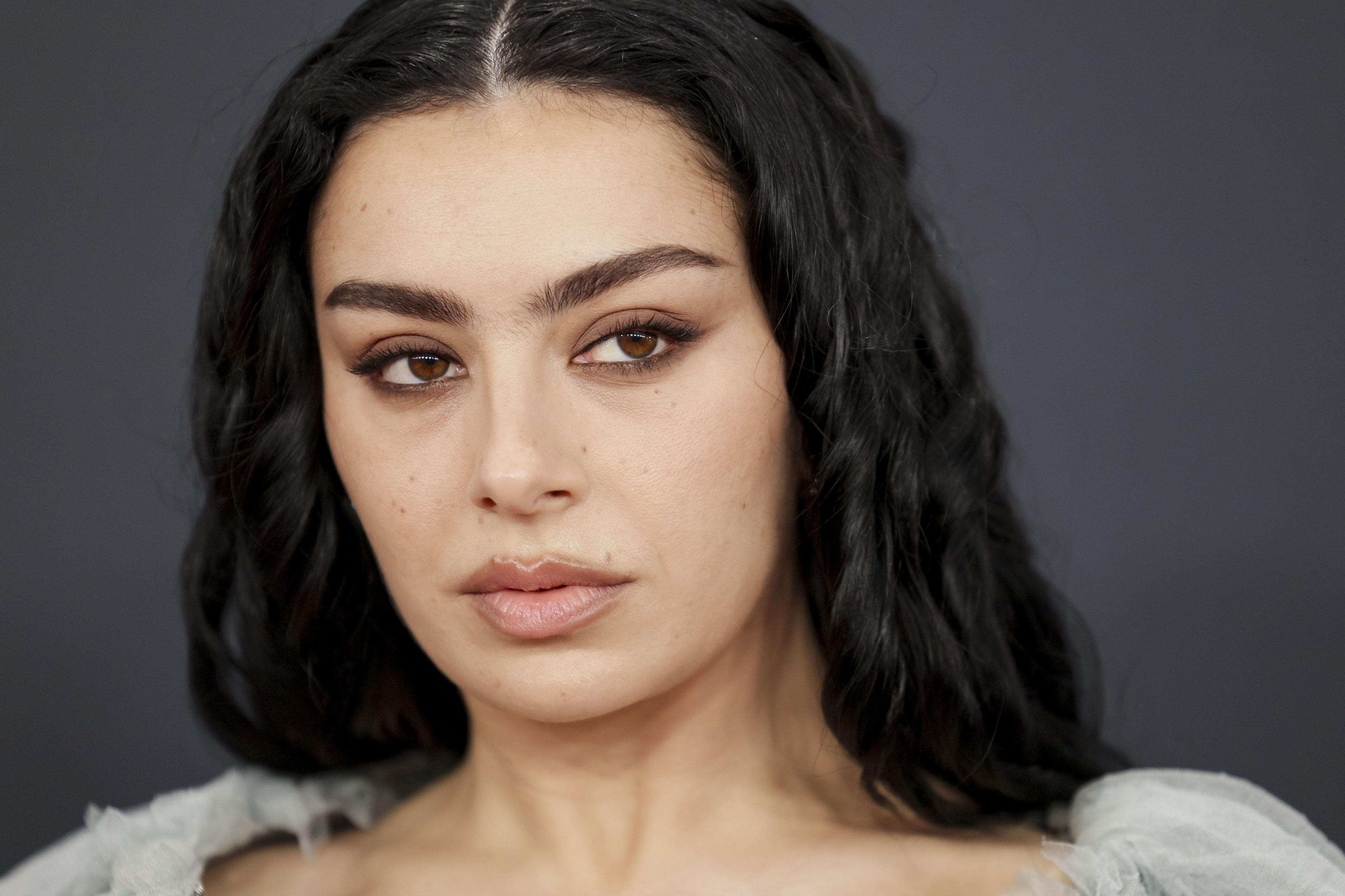 A close up shot of Pop star Charli XCX looks smouldering and pouts. She has brown eye shadow and clear skin on a red carpet.