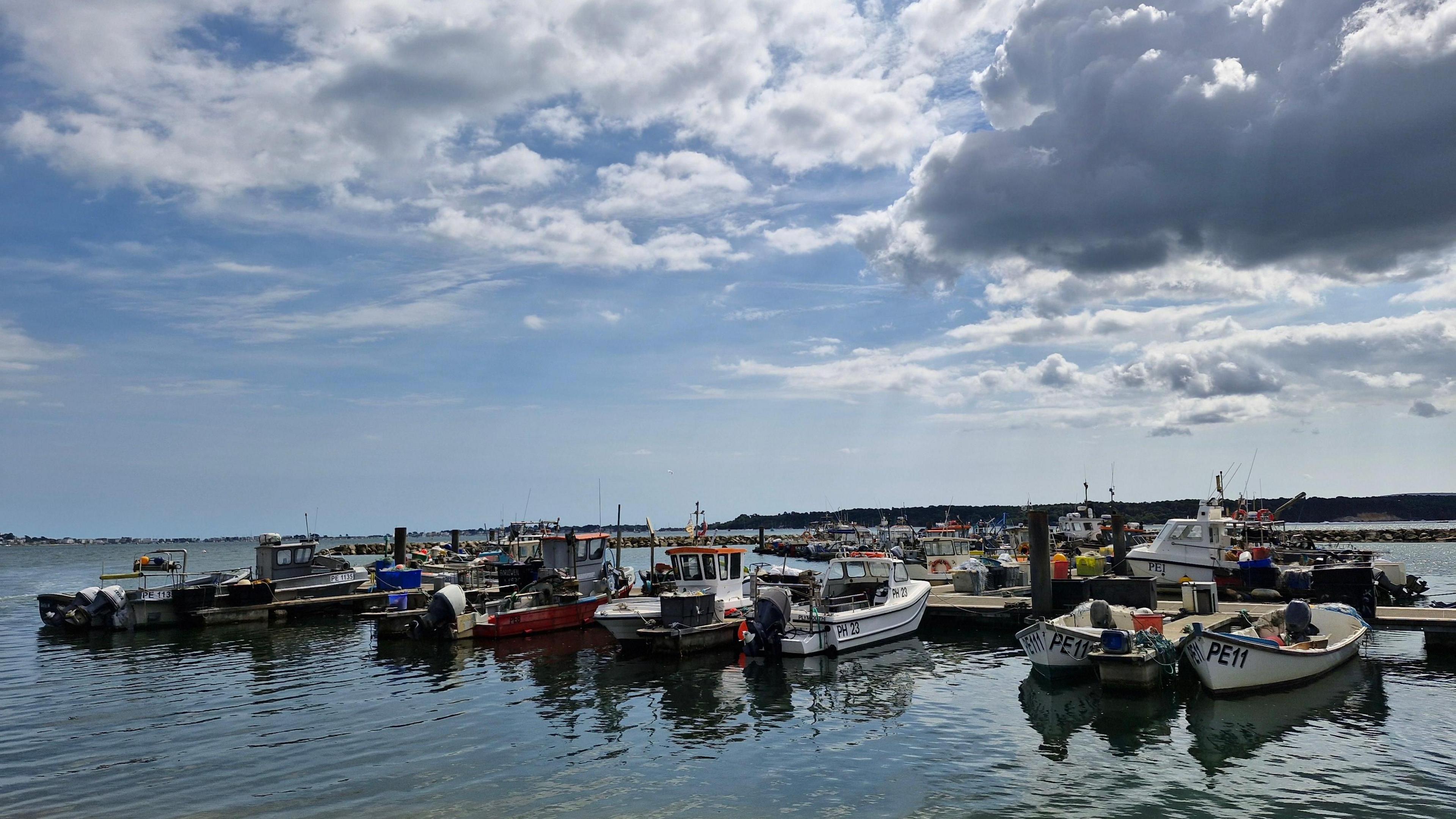 Eight small boats anchored in the foreground beneath a sky with a mix of blue and cloud
