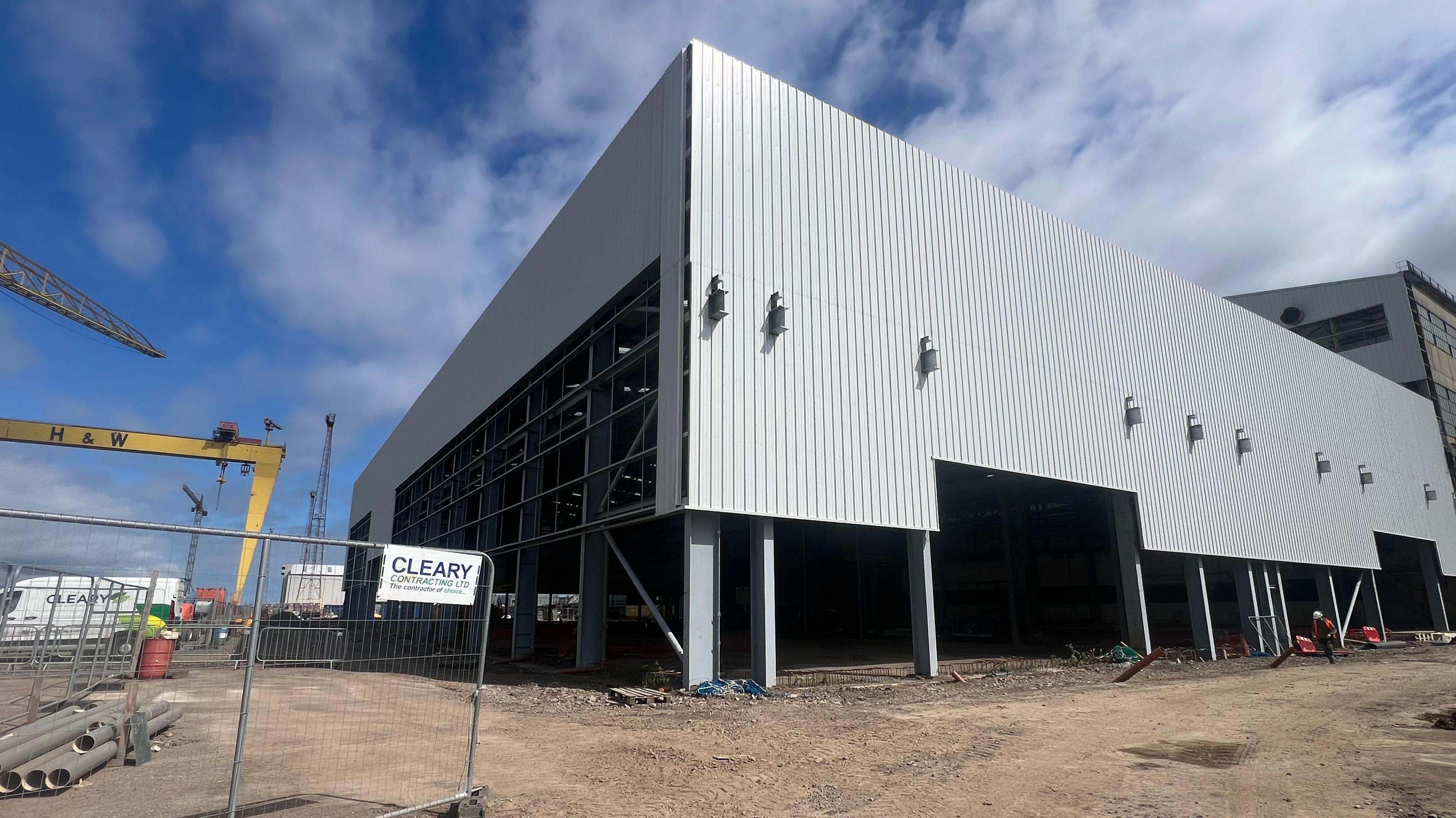 A wideshot of the tin warehouse which will be used to store components at Harland and Wolff's shipyard. In the distance are the two, iconic yellow cranes displaying H&W in large black letters.