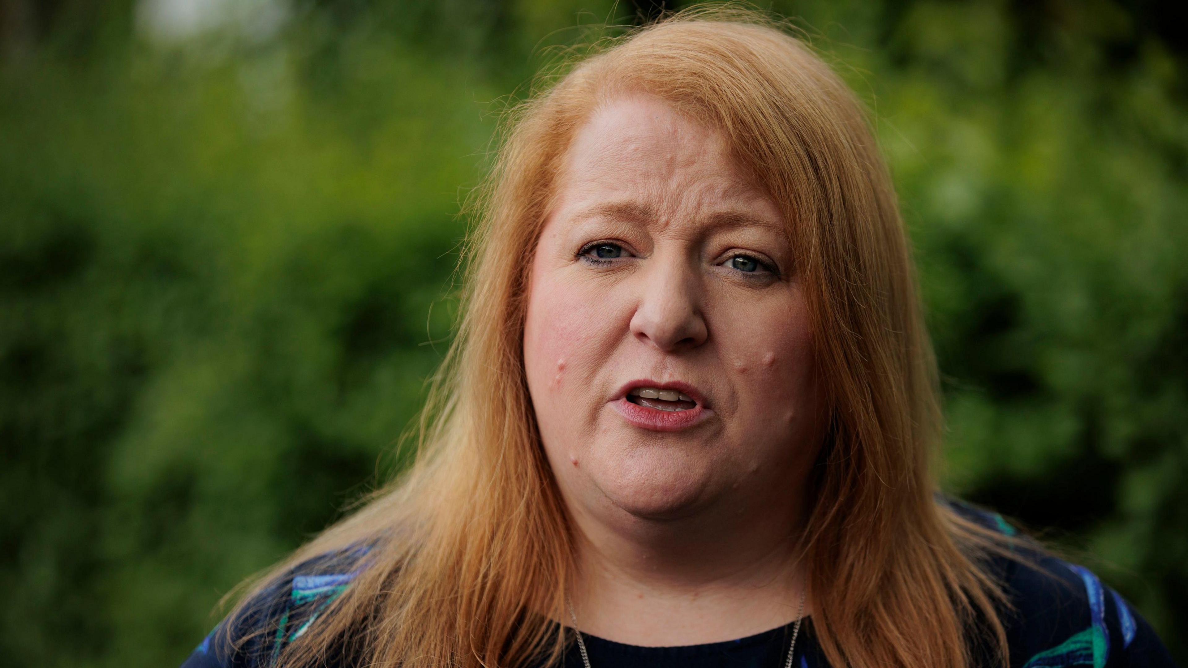 Naomi Long - a woman with medium-length ginger hair wears a floral top.