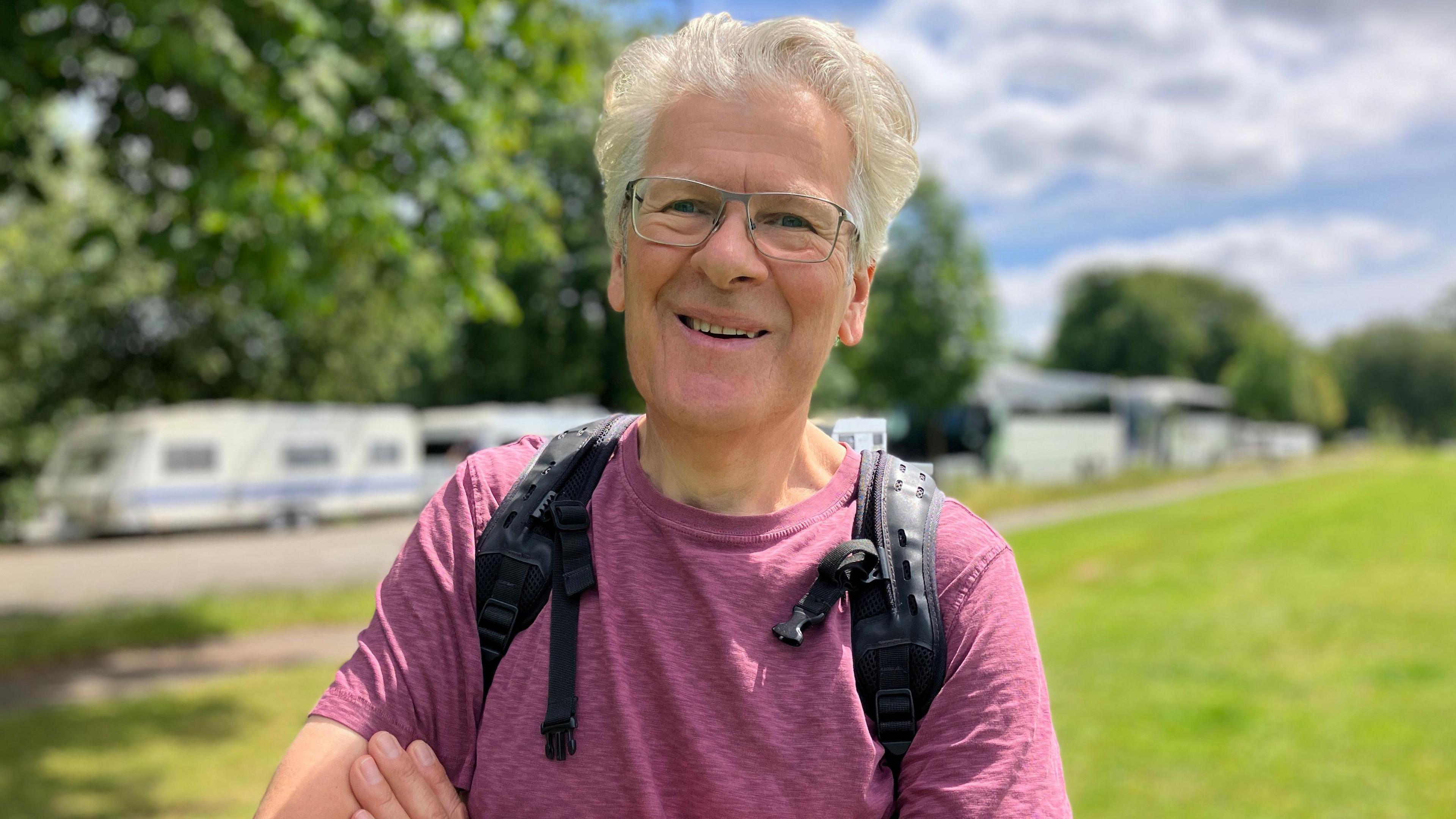 Chris Leeks. He is pictured outside, with a row of caravans behind him. He has white hair and glasses. 