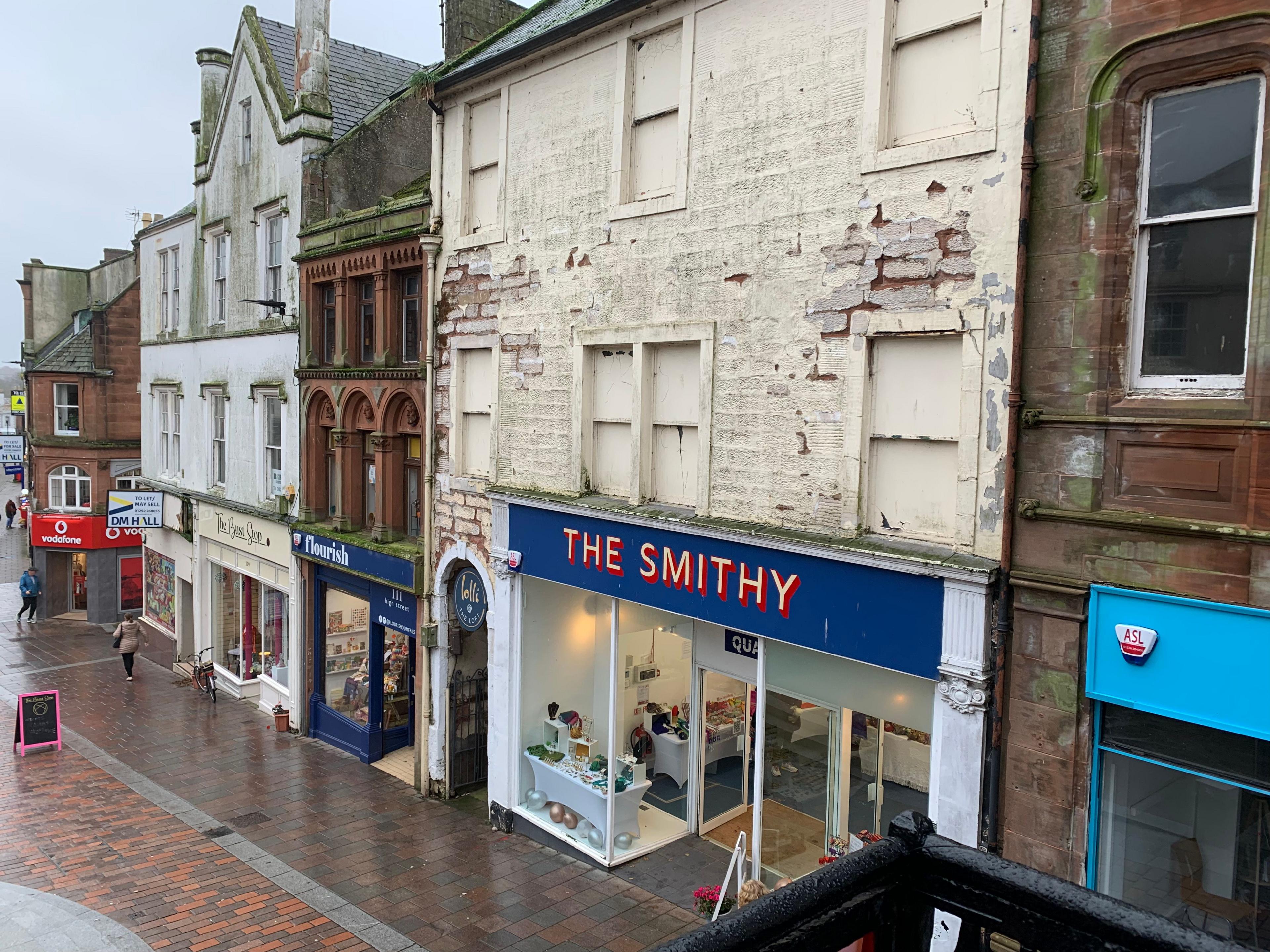 A row of dilapidated buildings with new shop fronts on some of them on a dreary day in Dumfries