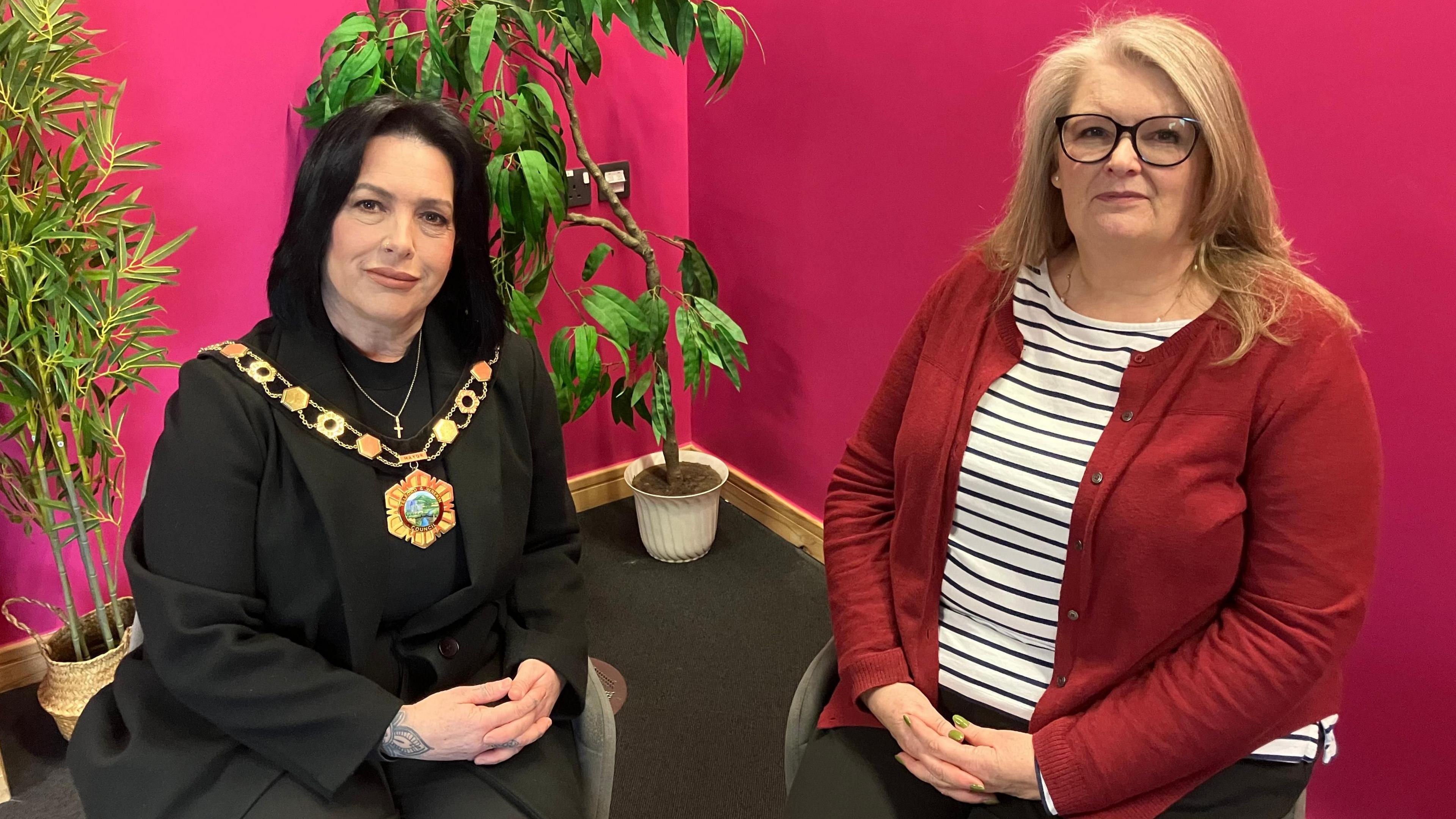 Councillor Eileen Callear, Telford and Wrekin Mayor and Jane Lees, town clerk for Hadley and Leegomery Parish Council sitting together in front of a pink wall with green plants in the background.  Both looking into the camera. 
