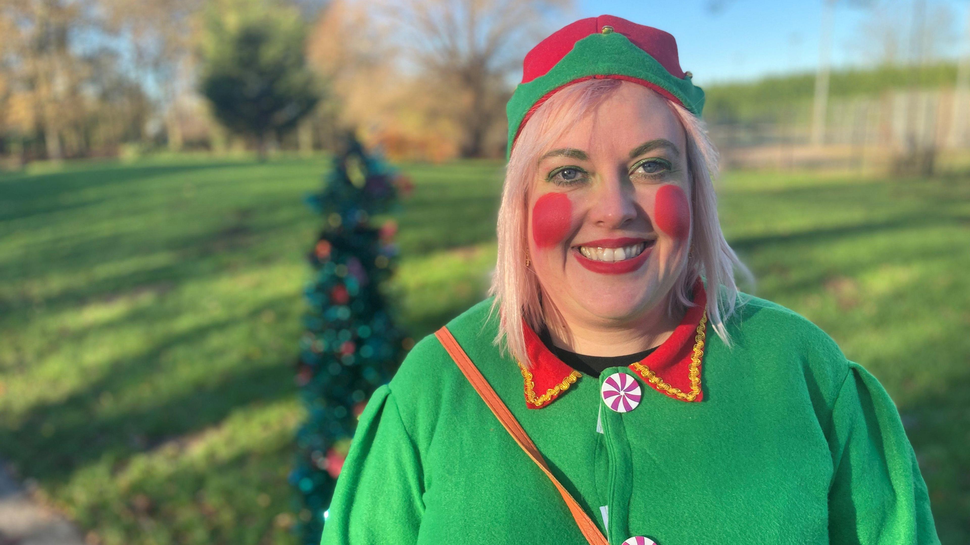 Chloe has a full bright green elf costume on and has complete the look with big red apple cheeks and red lipstick.