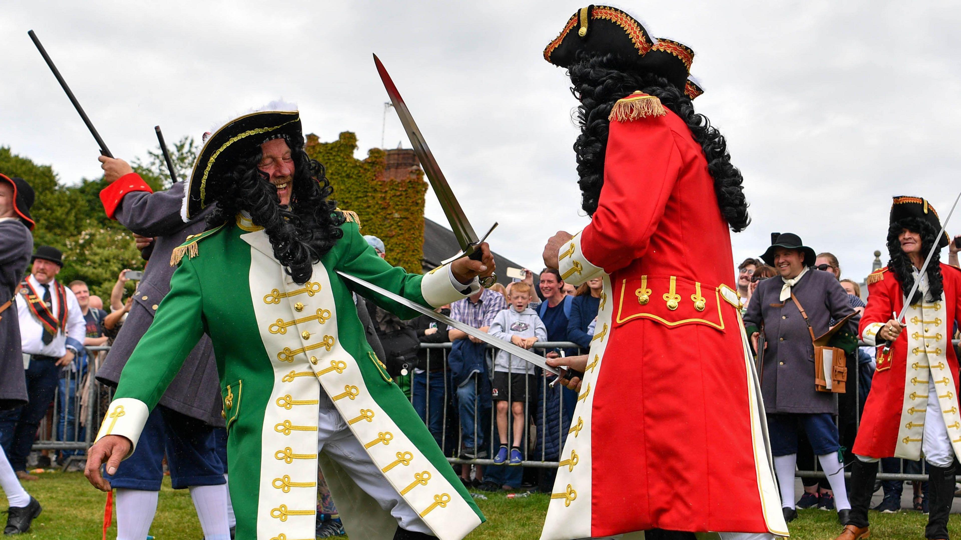 King William's actor wearing a red military coat pretends to stab King James, wearing a green coat, with a sword signalling the victory