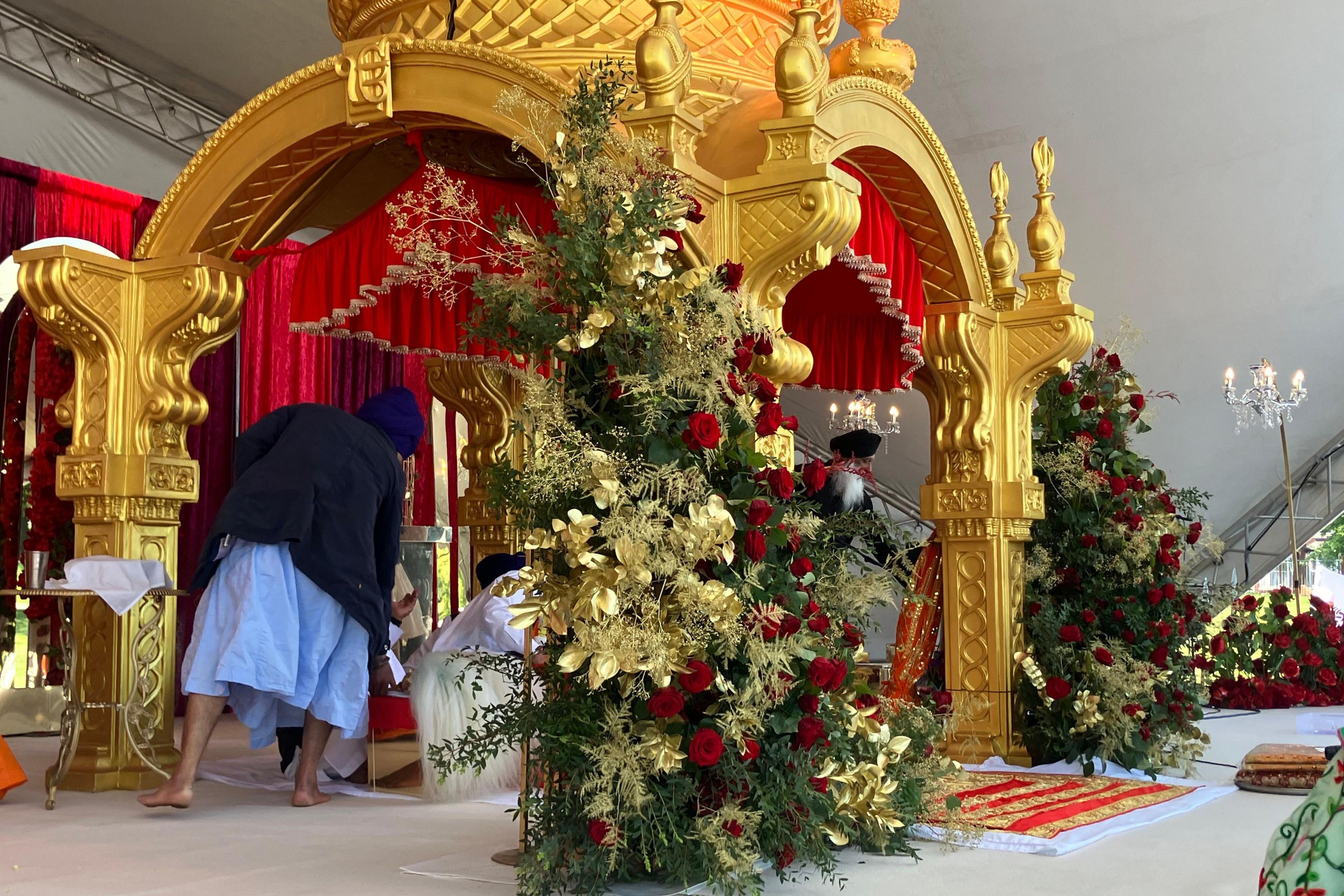 A large golden monument decorated with gold and red flowers next to the front two pillars. A man can be seen leaning towards the middle of the ornate gold structure.