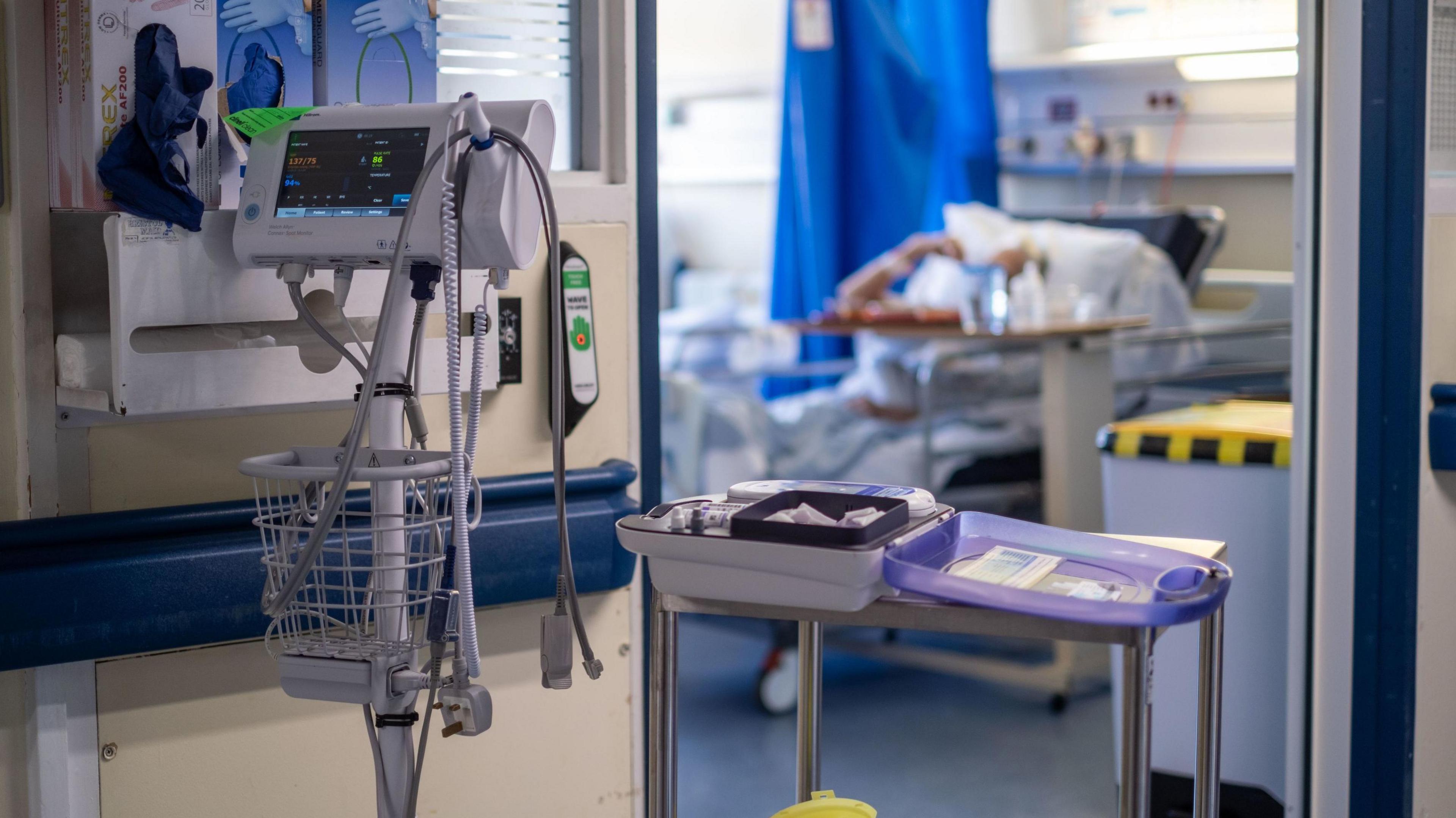 A general view into a hospital room with a patient lying in a bed and medical equipment in the foreground