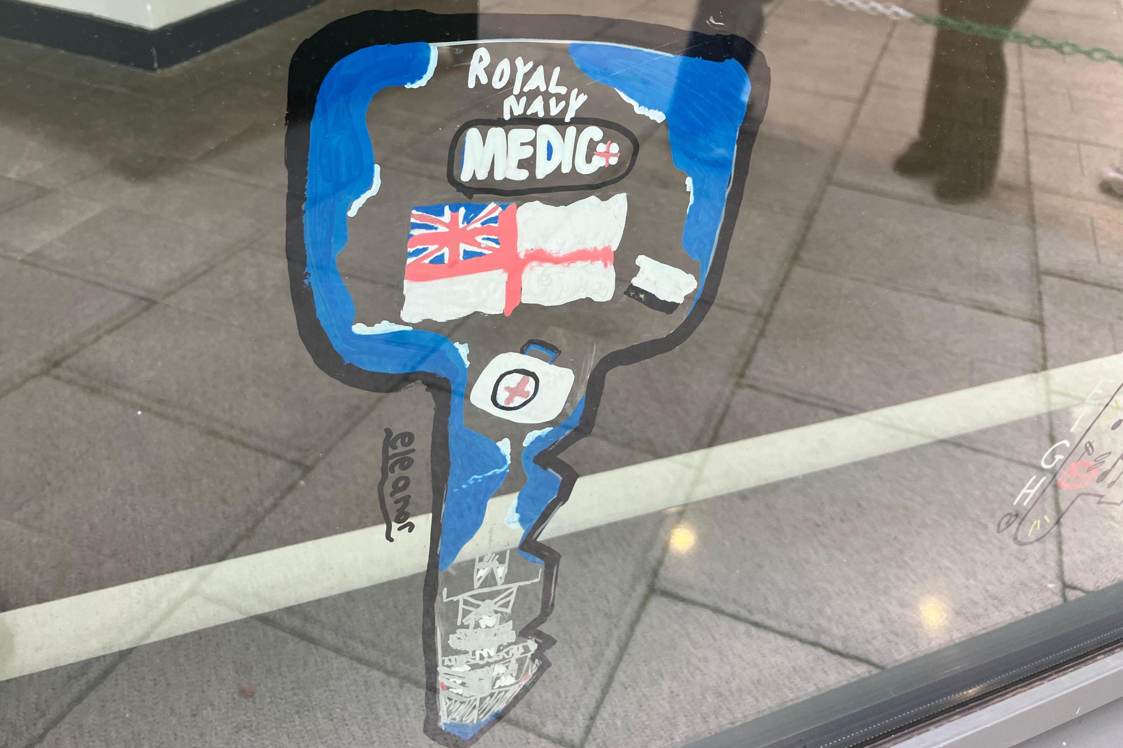 A large key-shaped outline painted on a glass window. Inside the shape is written Royal Navy medic, with blue outline, a navel flag and a first aid kit.