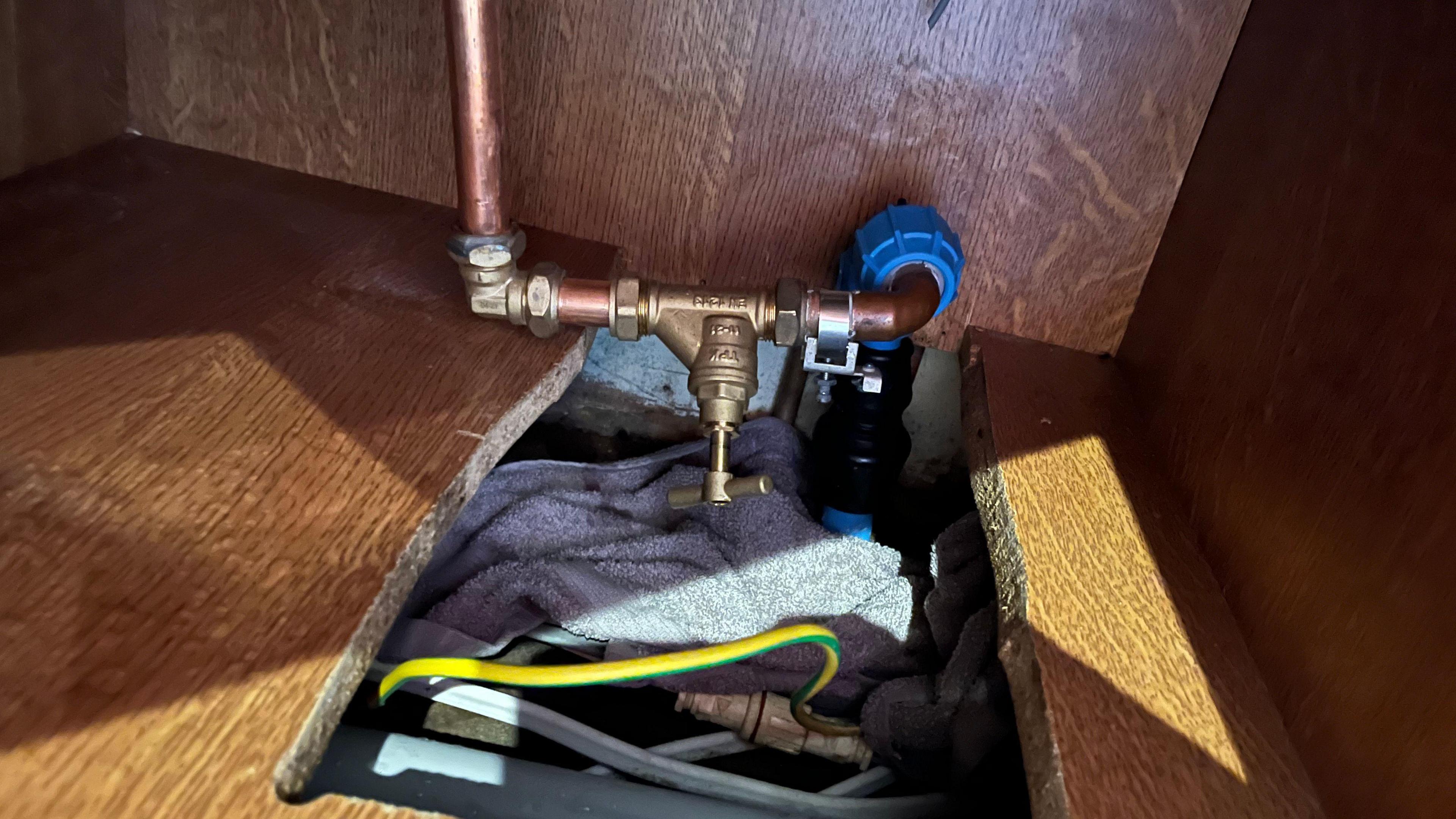 A water pipe in a cupboard over a rectangular hole