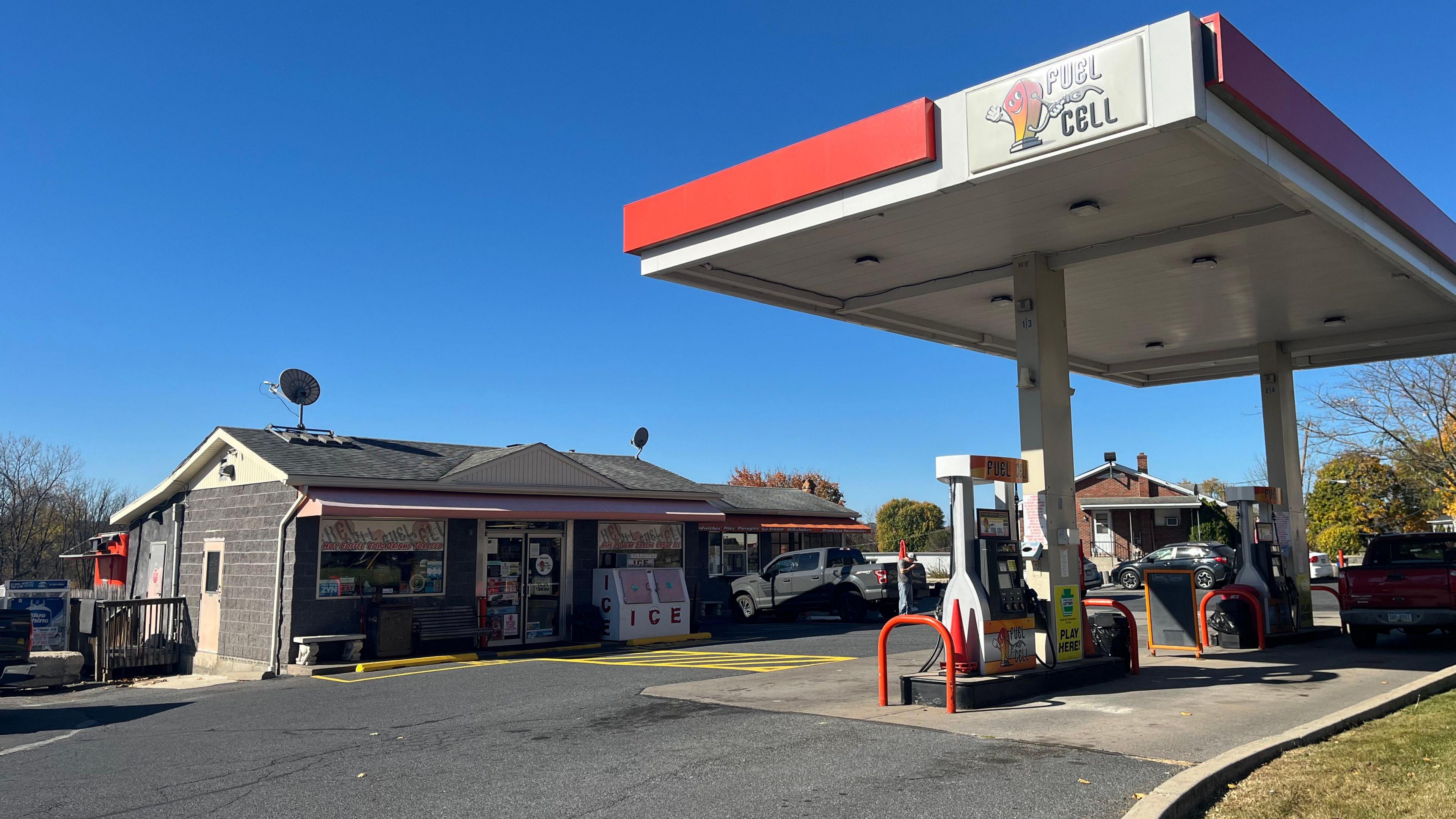 A gas station with a restaurant attached. There is a filling up station area and a building for the shop and diner. There's an ice box outside.