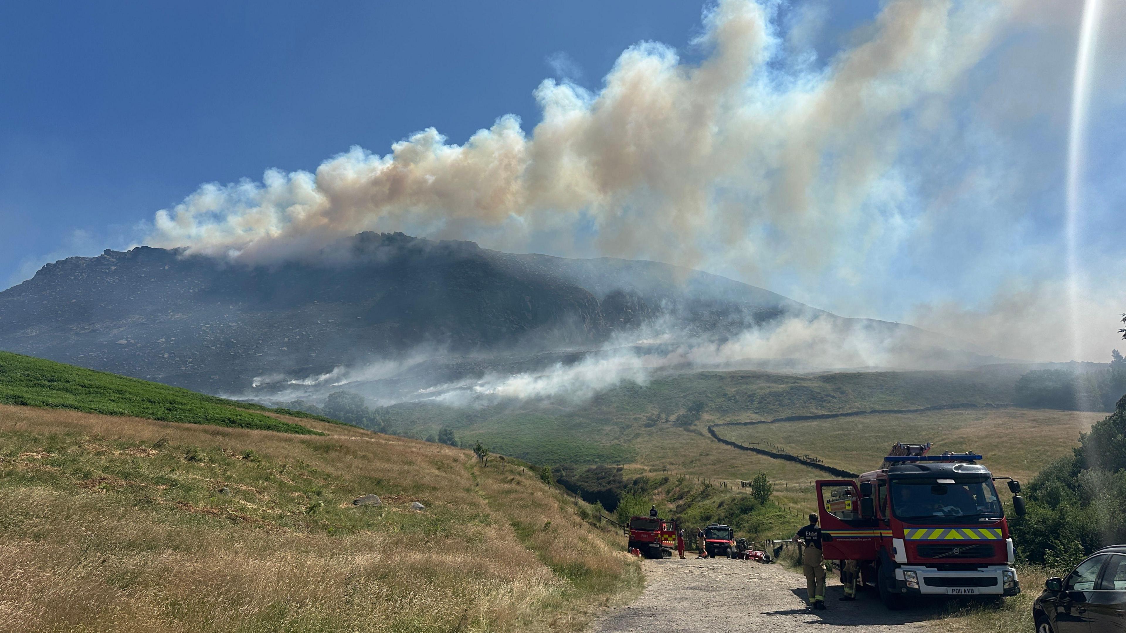 Three fire engines are parked up on a dirt track on the moors, with plumes of smoke seen billowing from the moors in the distance