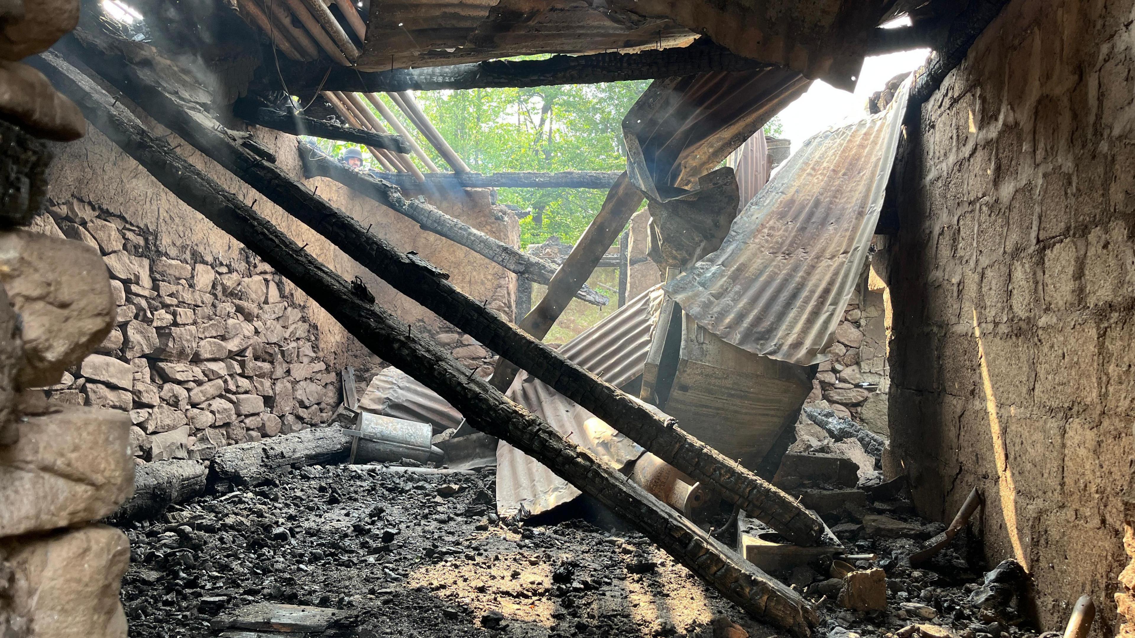 The inside of a ruined stone home, with the tin roof caved in