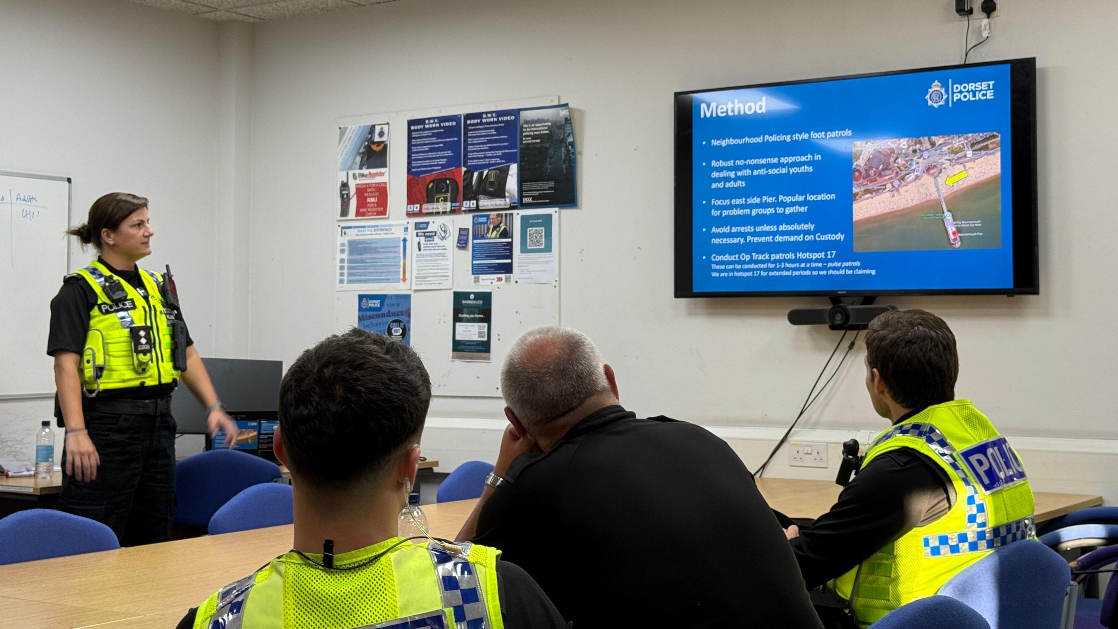 A group of police officers sat around a table looking at a screen.